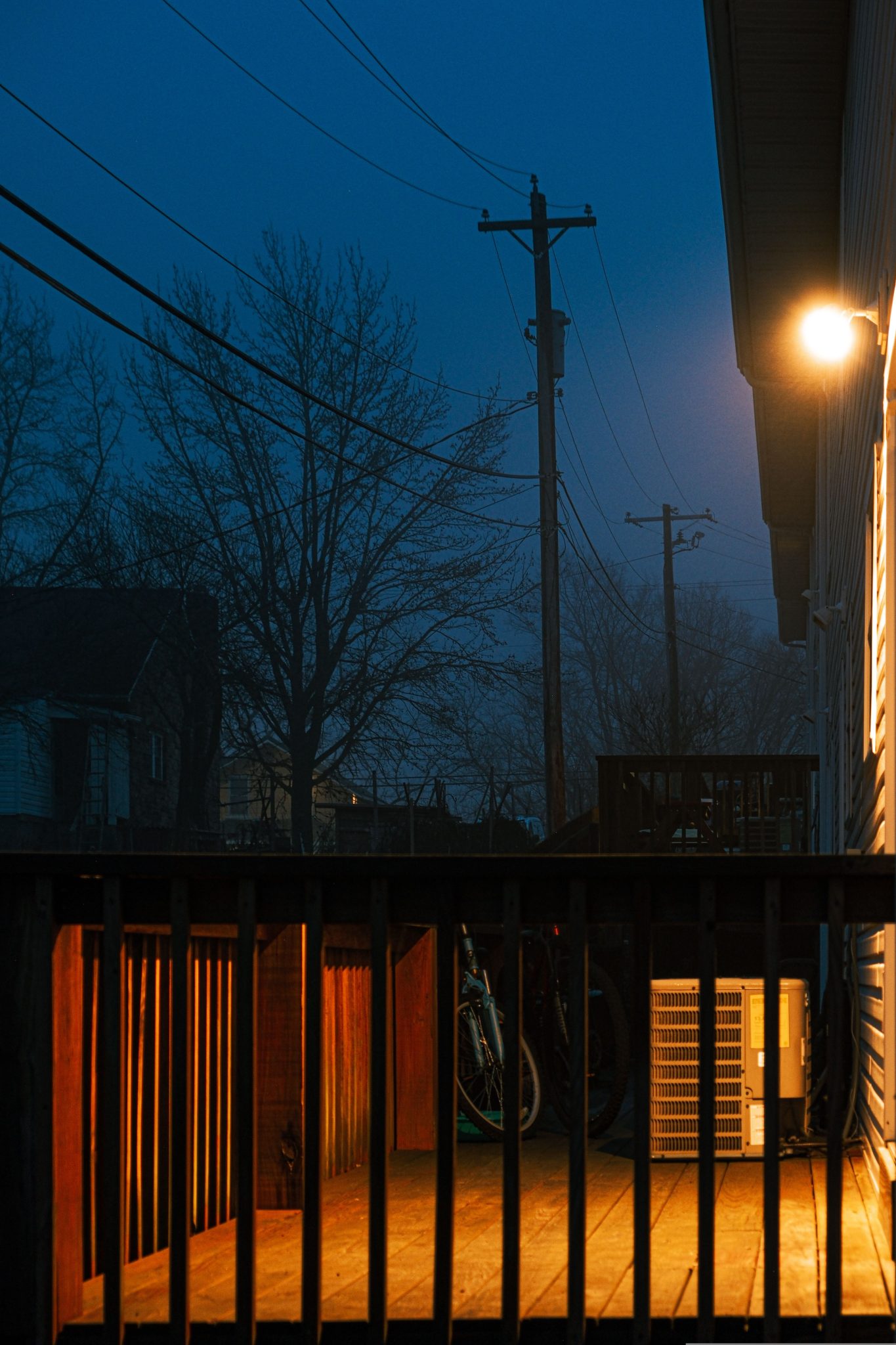 Warmly lit residential porch at night with urban trees and power lines.