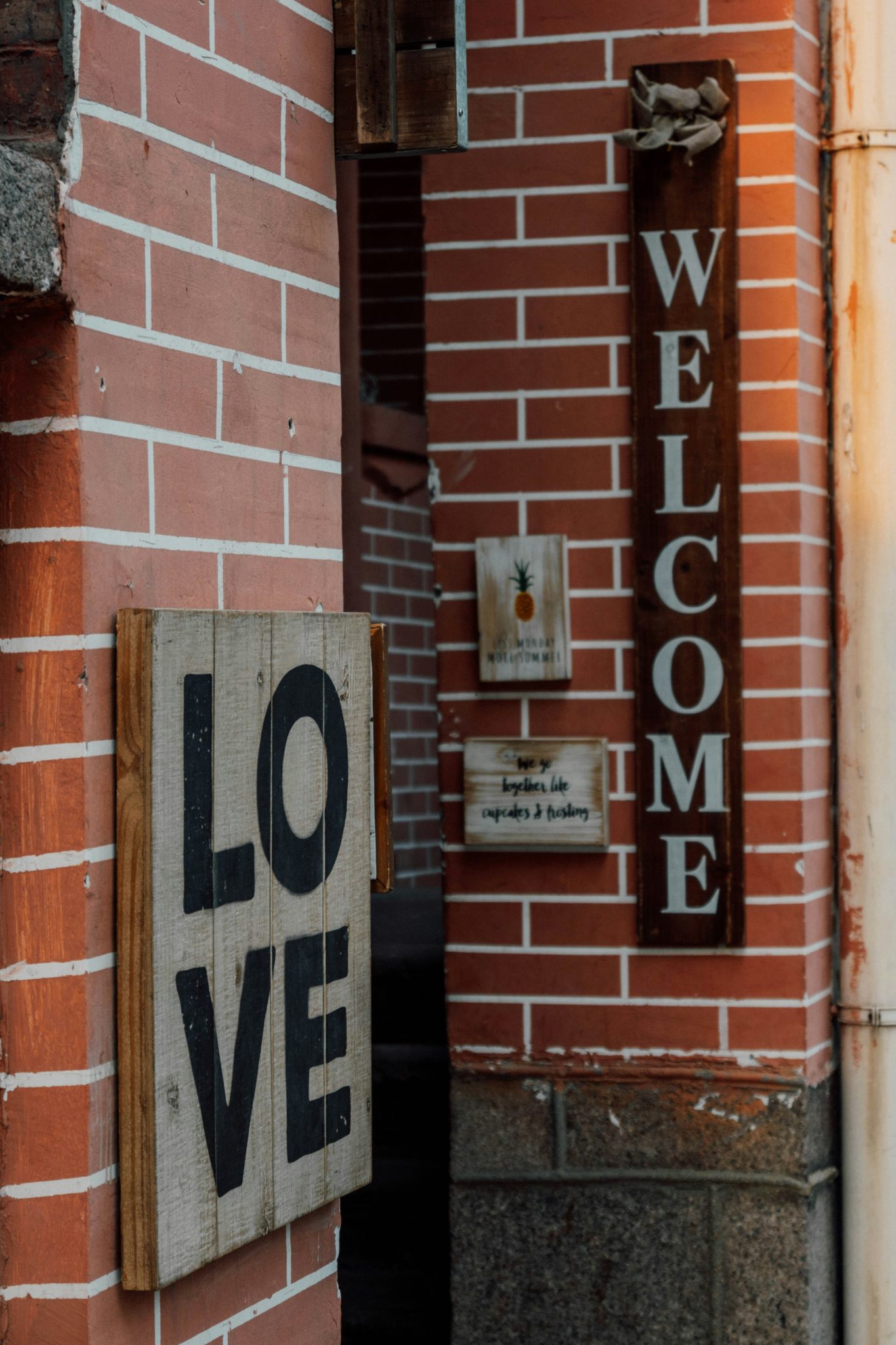 Wooden signs reading LOVE and WELCOME on a red brick wall