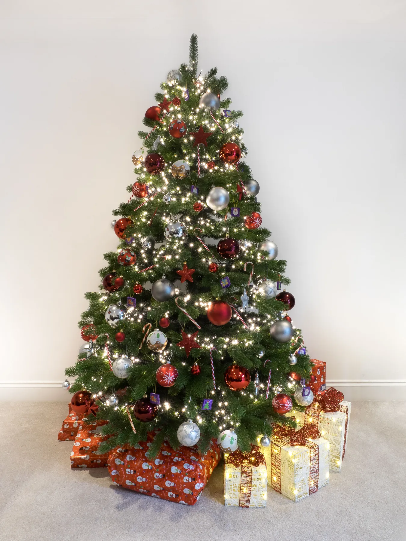 A beautifully adorned Christmas tree with colorful ornaments and sparkling lights surrounded by wrapped gifts on a white background.
