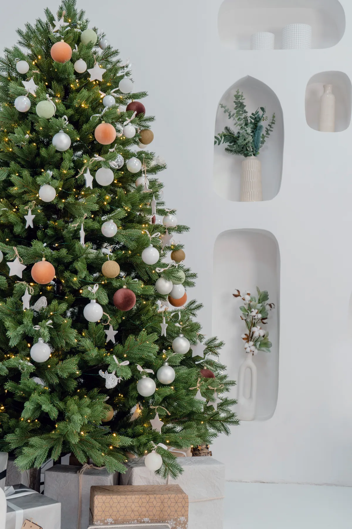 A beautifully decorated Christmas tree with gifts in a minimalist white room, exuding festive charm.