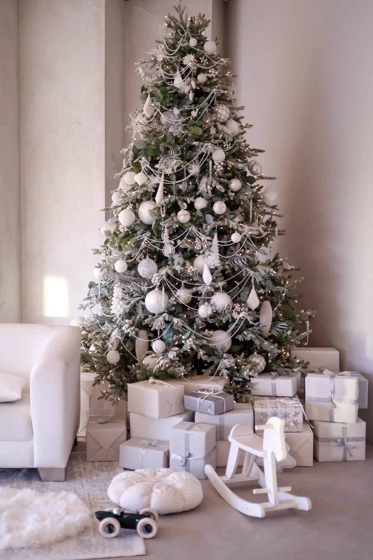 A beautifully decorated Christmas tree with wrapped gifts and a rocking horse in a cozy living room.