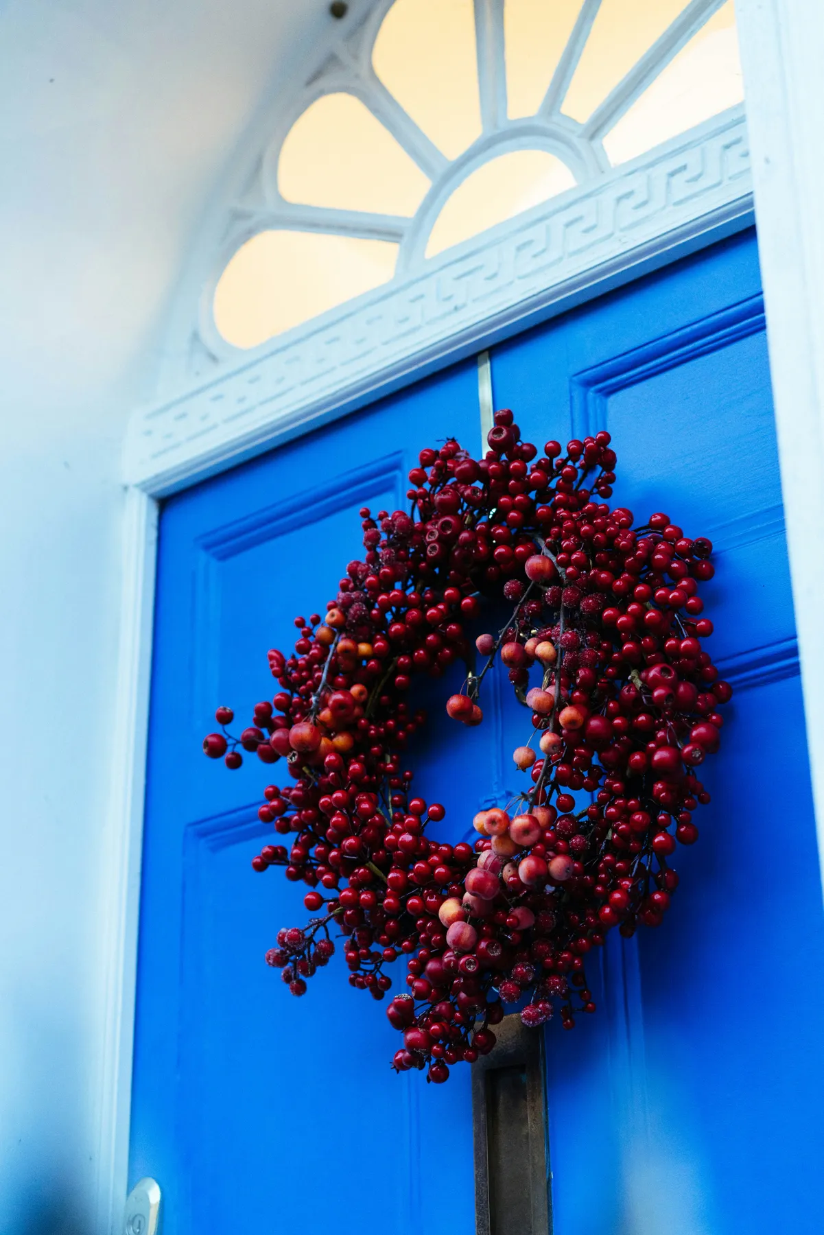 A bright blue door with a red berry wreath