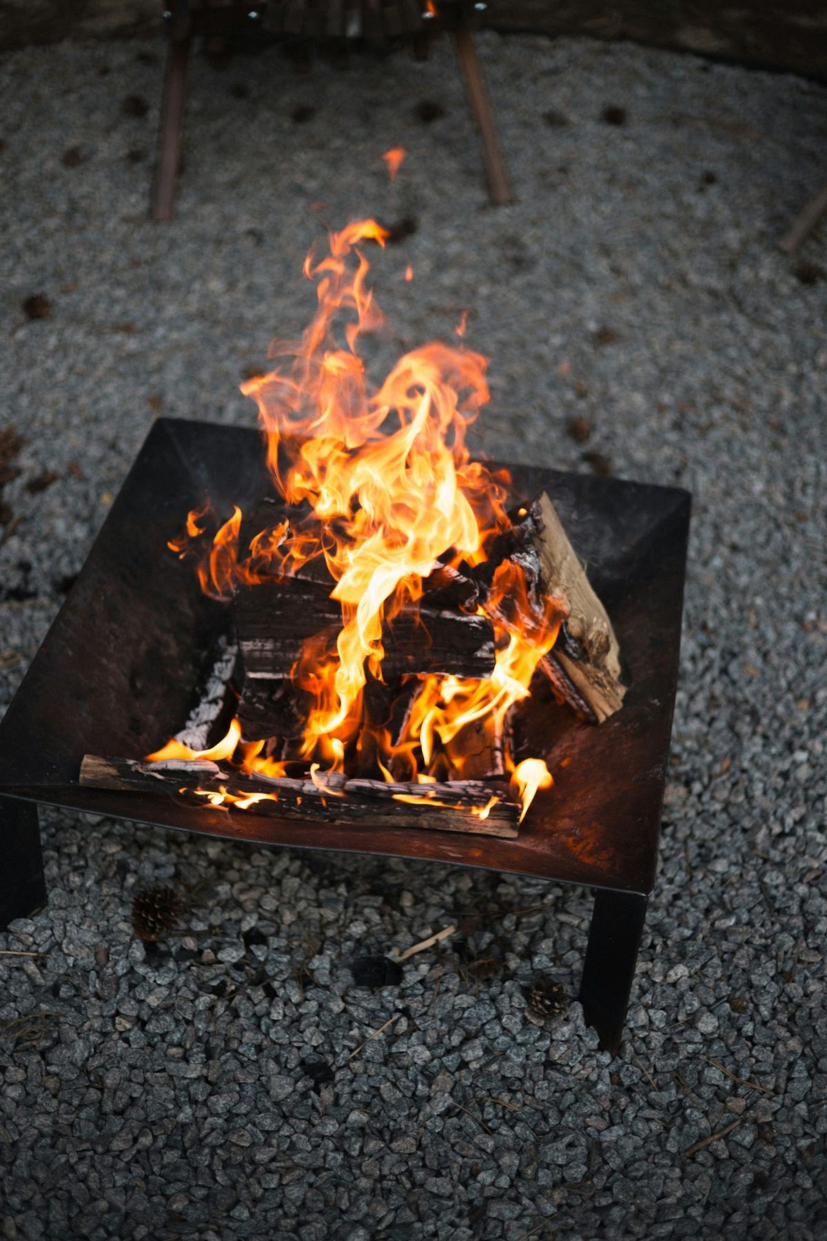A bright fire burning in a metal fire pit on grey gravel