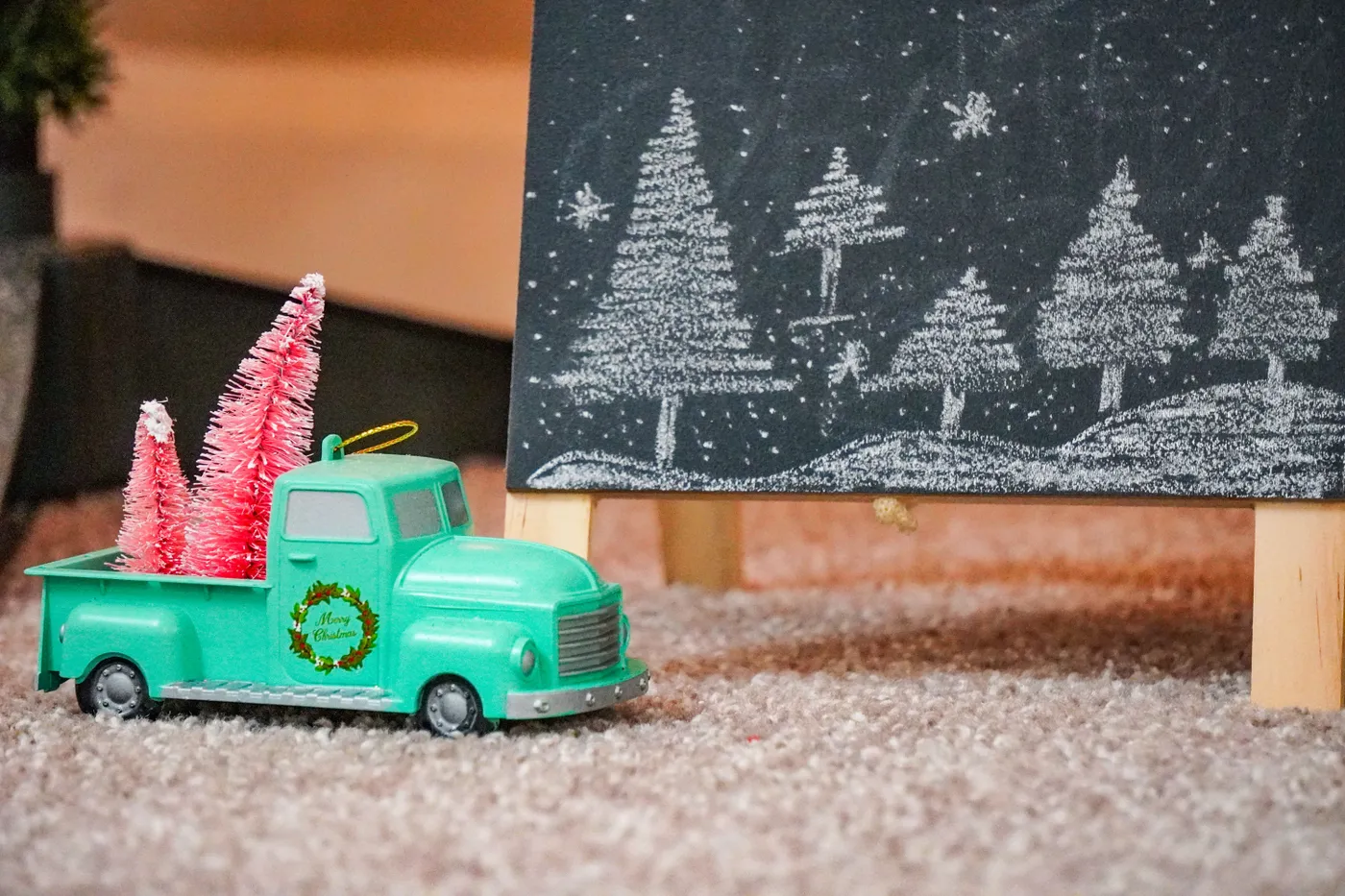 A charming holiday scene featuring a toy truck with pink trees and a chalkboard Christmas drawing.