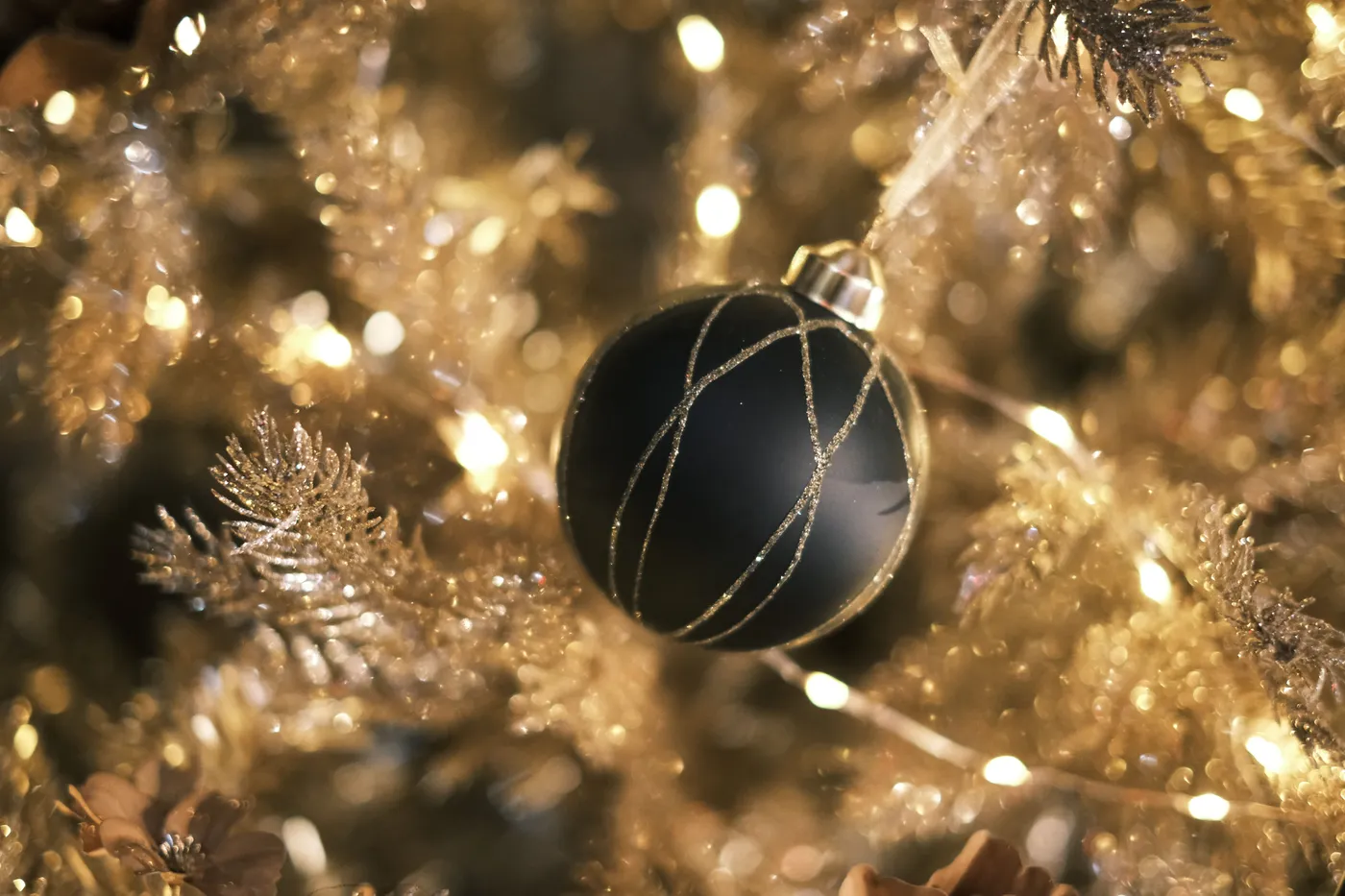 A close-up of a black Christmas ornament hanging on a shimmering gold Christmas tree, beautifully lit.