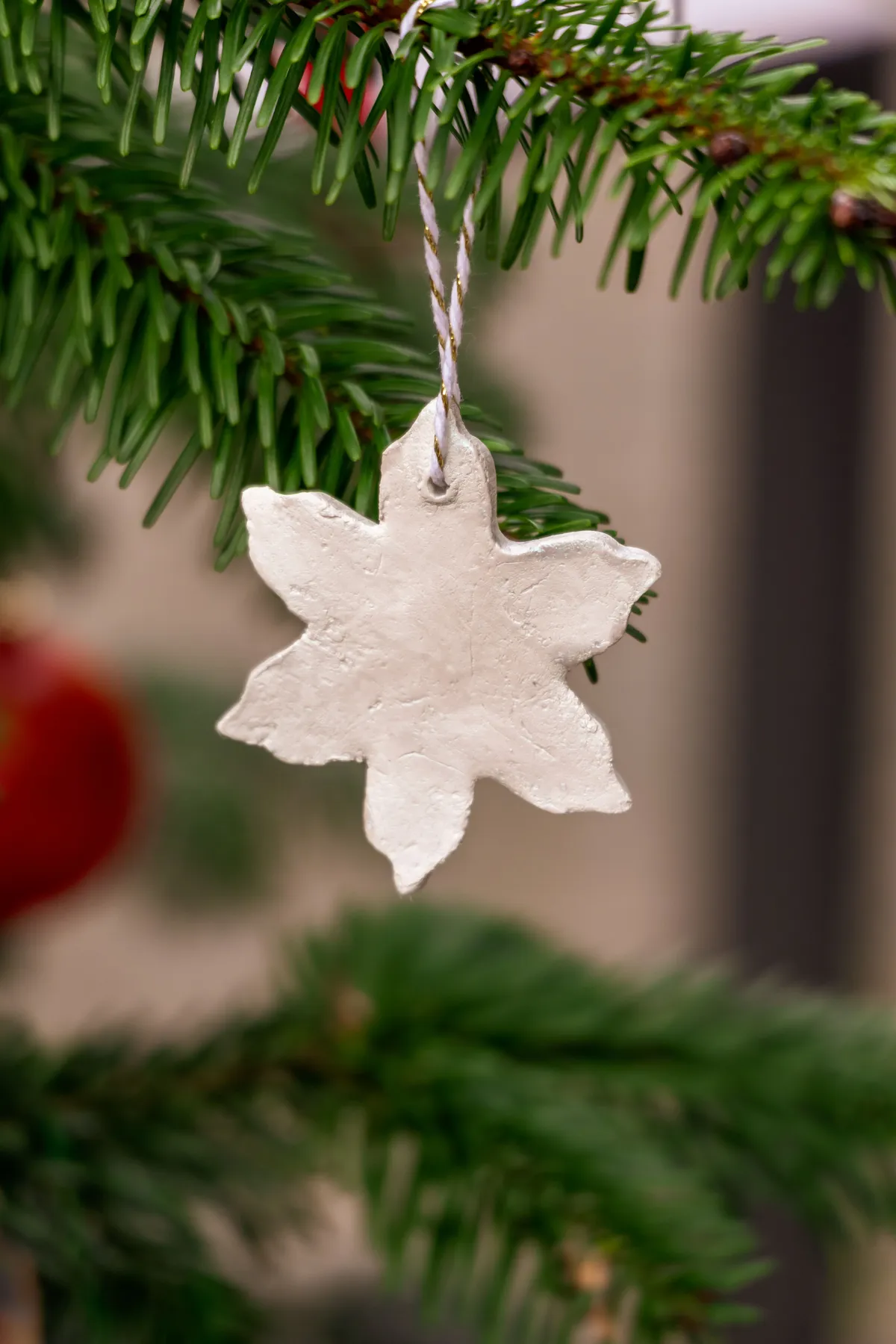 A close-up of a handmade clay snowflake ornament hanging on a pine tree branch, perfect for festive decor.