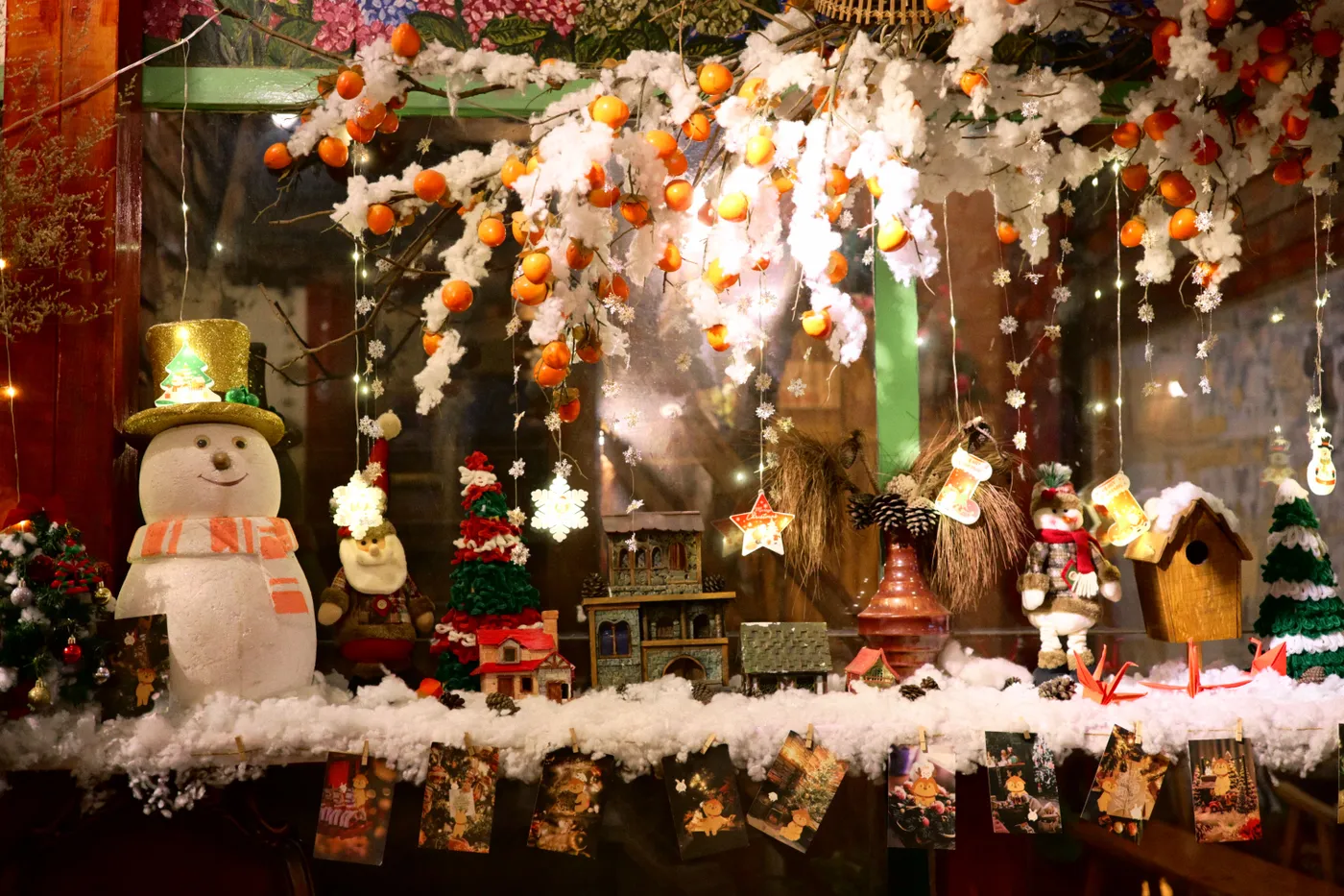 A colorful, festive window display featuring a snowman, Christmas ornaments, and holiday decorations.