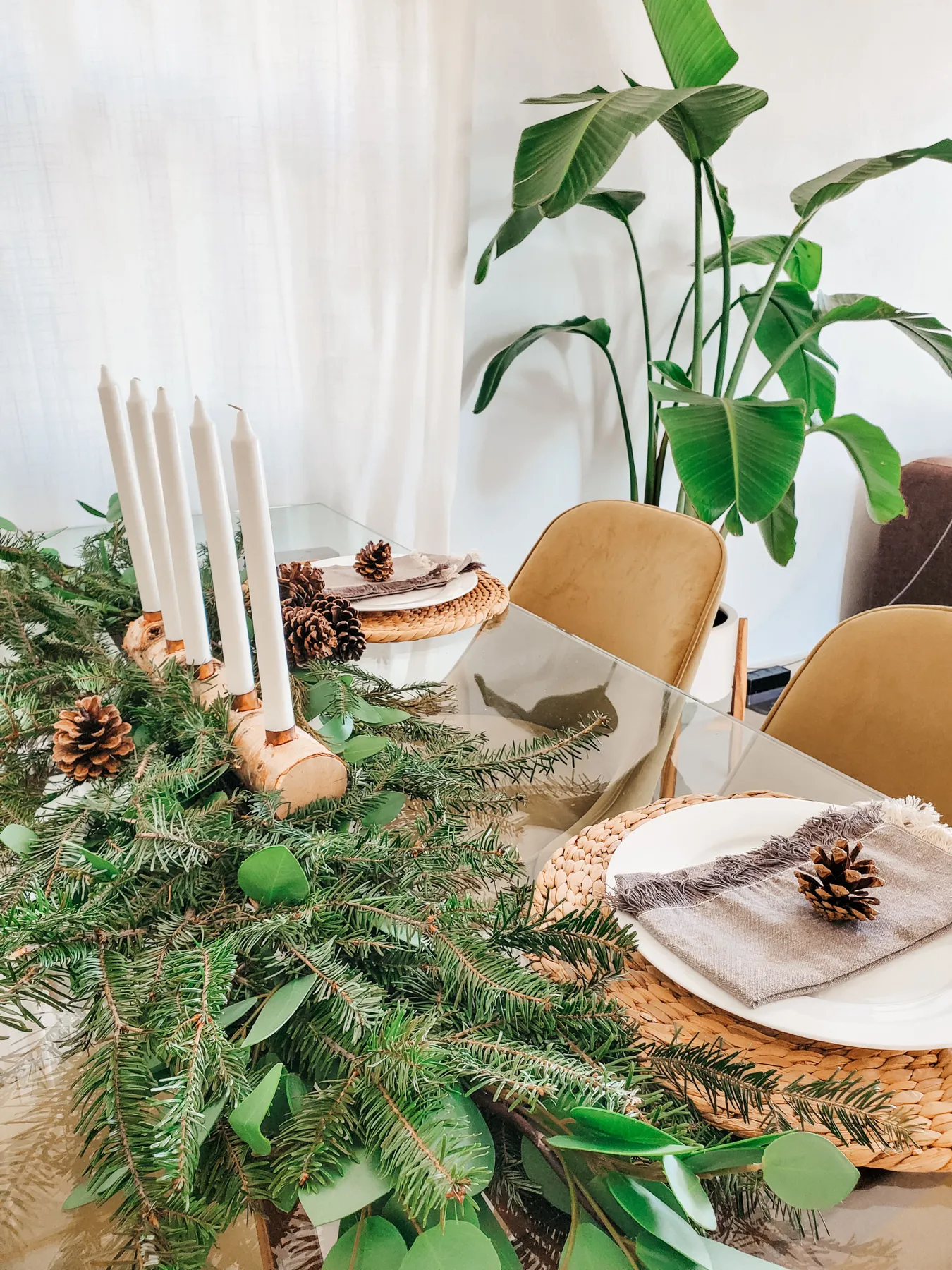A cozy Christmas tablescape with candles and pine decor.