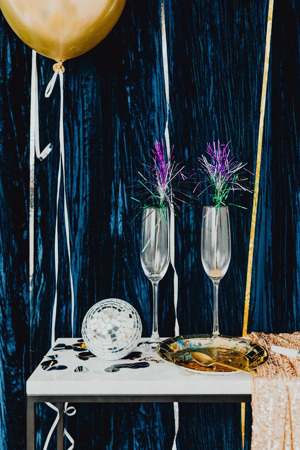 A festive New Year's Eve table setting featuring champagne glasses, a disco ball, and decorations.
