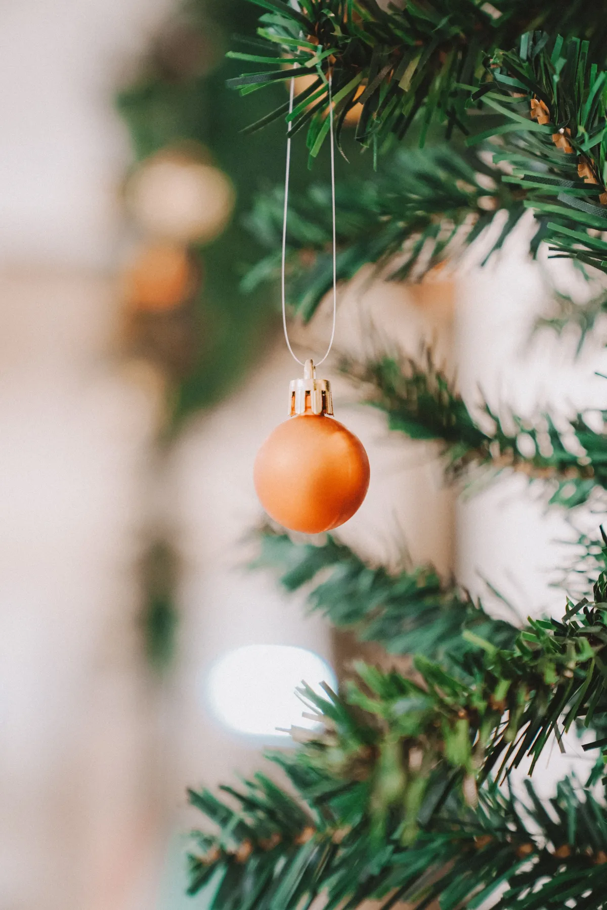 A festive orange bauble hanging on a Christmas tree branch indoors, perfect for holiday decor.