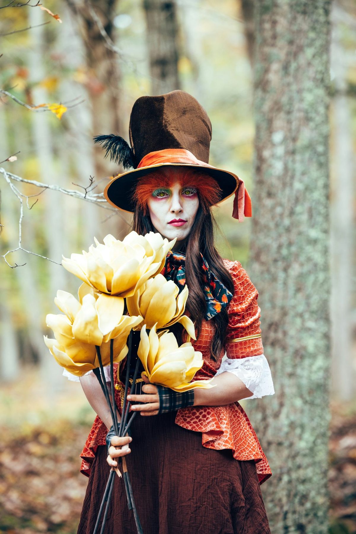 A person in a mad hatter costume holds yellow flowers