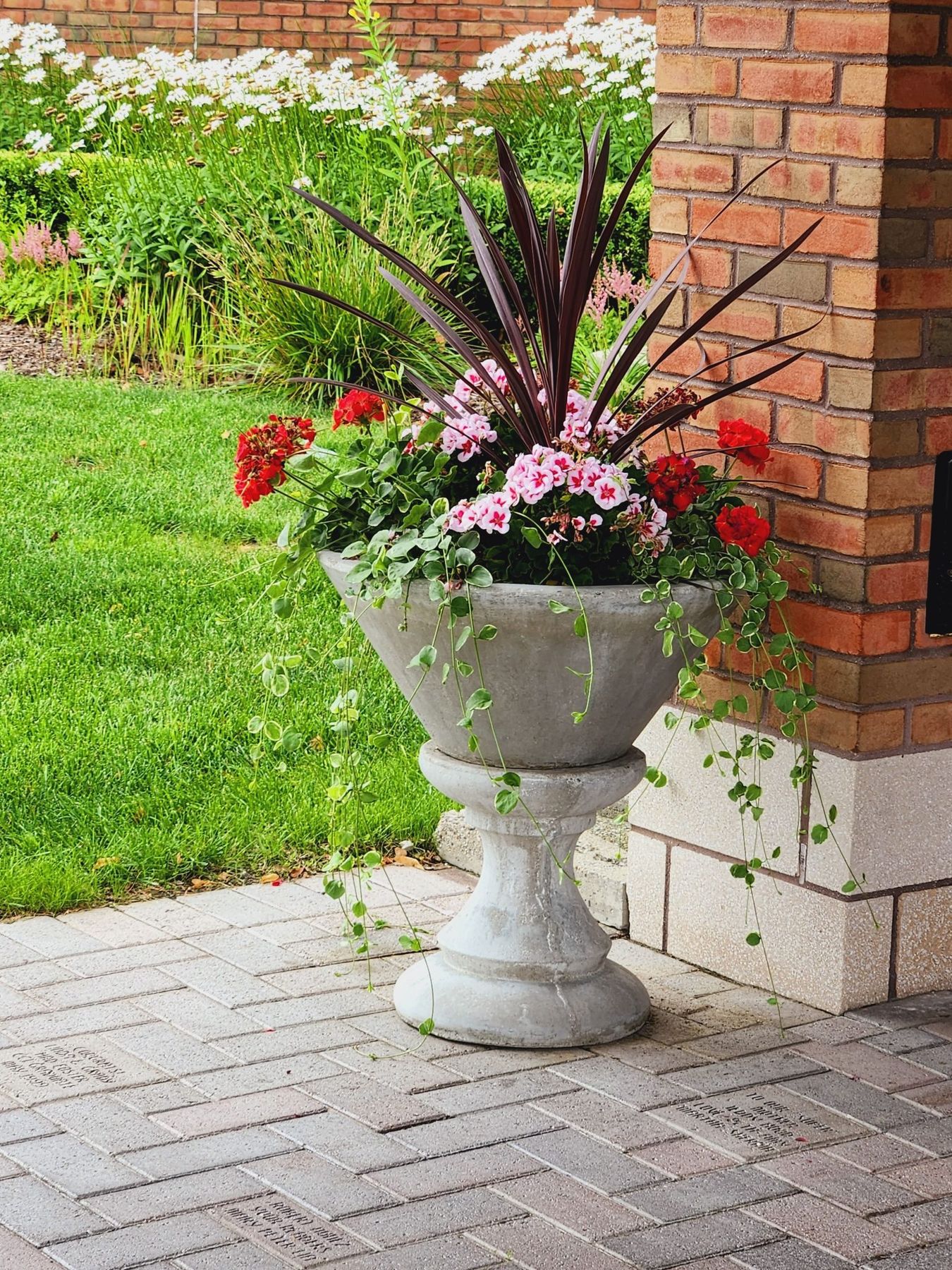 A stone planter filled with vibrant red and pink flowers and foliage against a brick wall, ideal for garden design inspiration.
