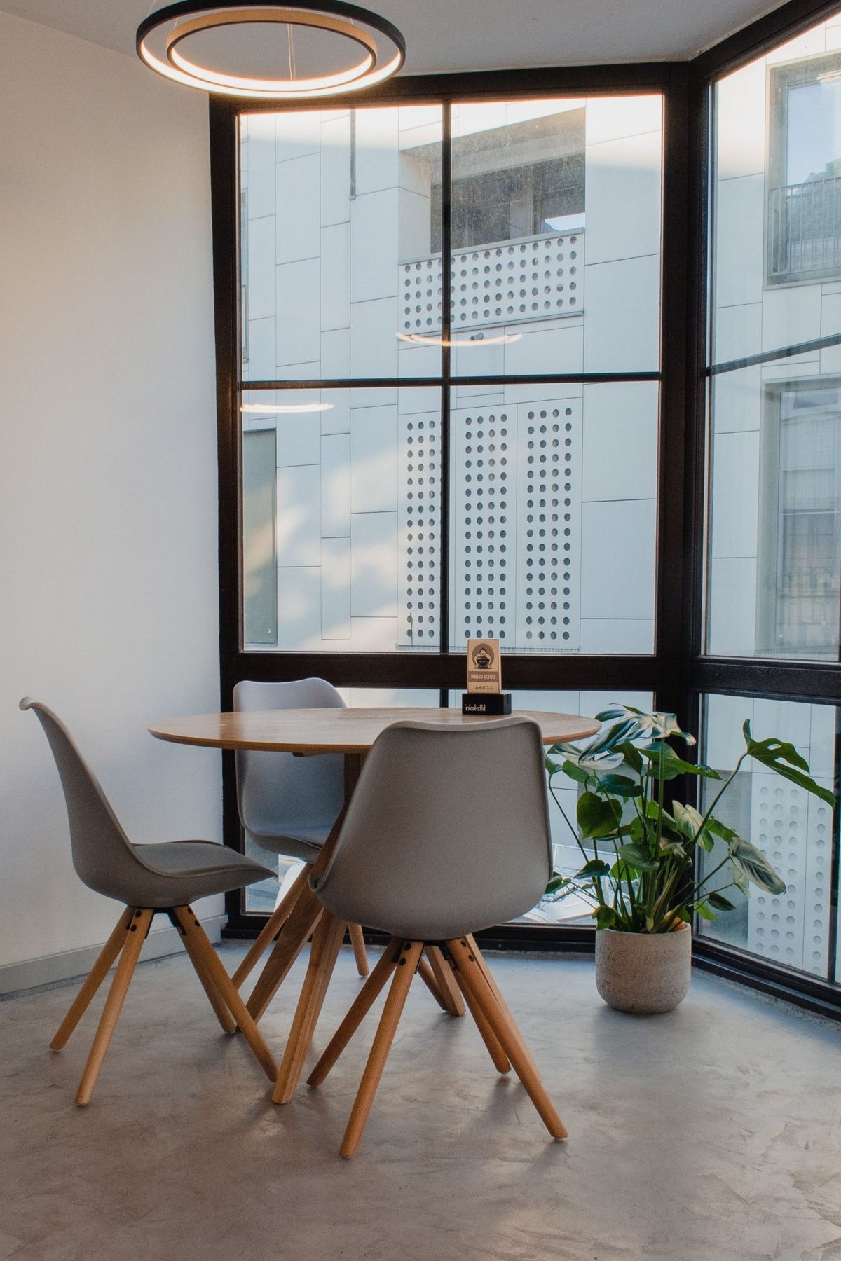 A stylish corner office space with a round table, three chairs, and a potted plant.