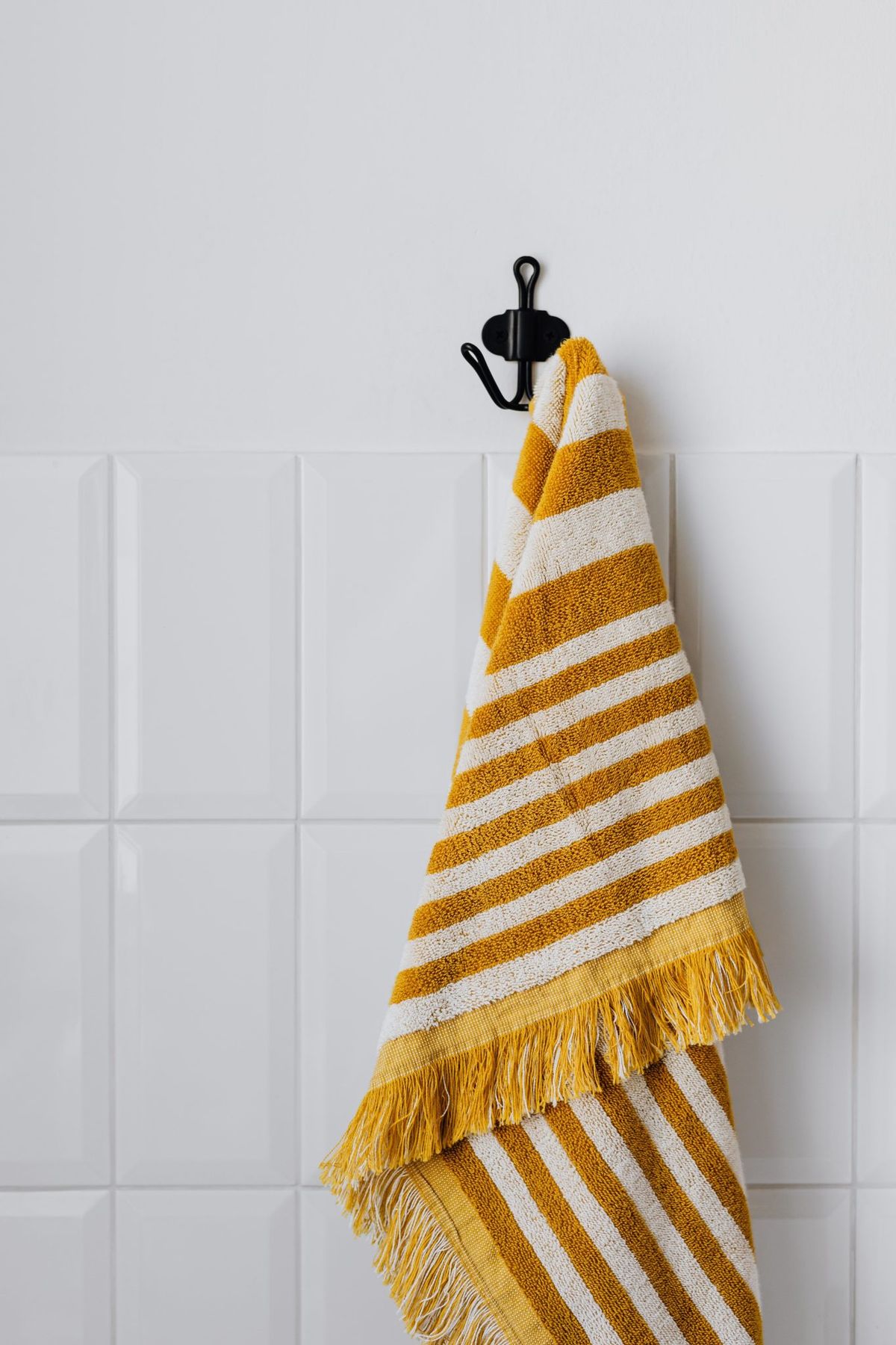 A stylish striped yellow and white towel hanging on a wall hook in a bathroom setting.