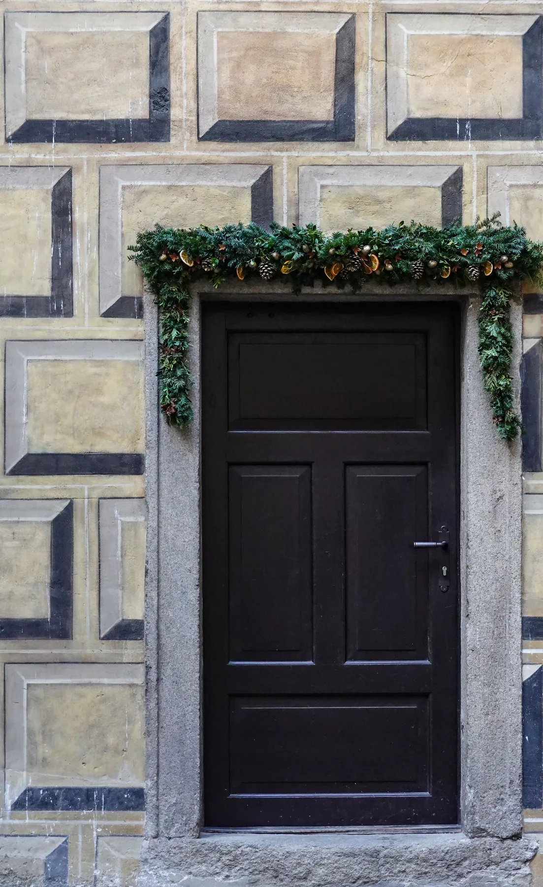 A traditional wooden door adorned with a festive Christmas garland featuring seasonal decorations.