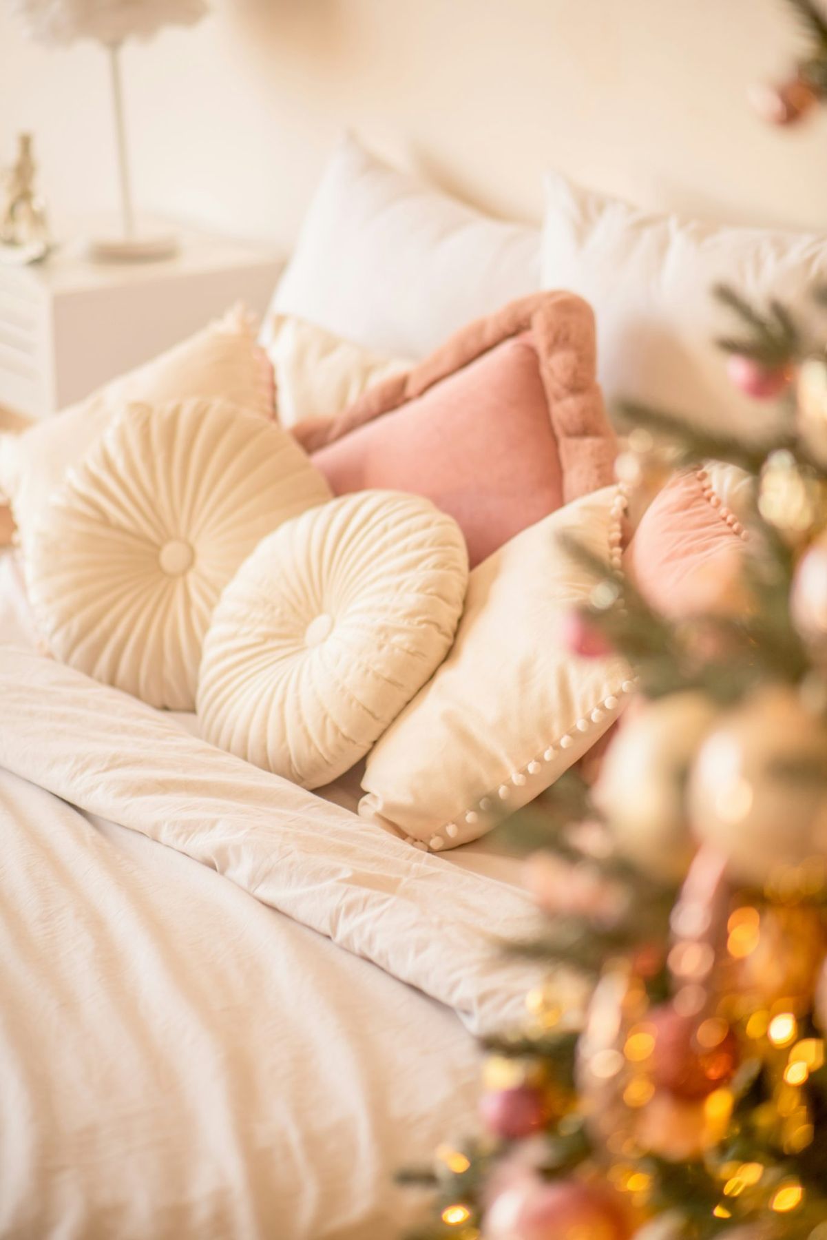 a white bed topped with lots of pillows next to a christmas tree
