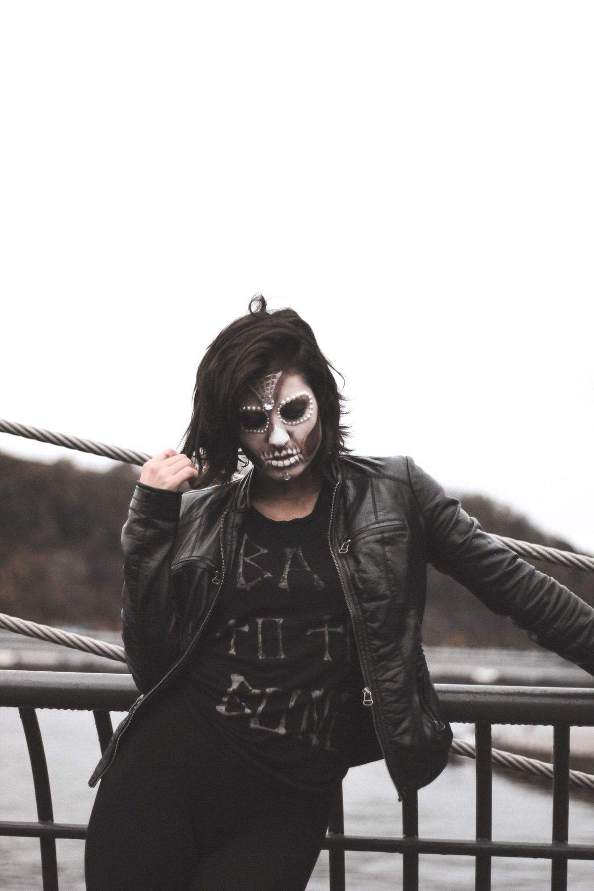 A woman with gothic face paint posed outdoors in a black leather jacket, adding mystery and allure.