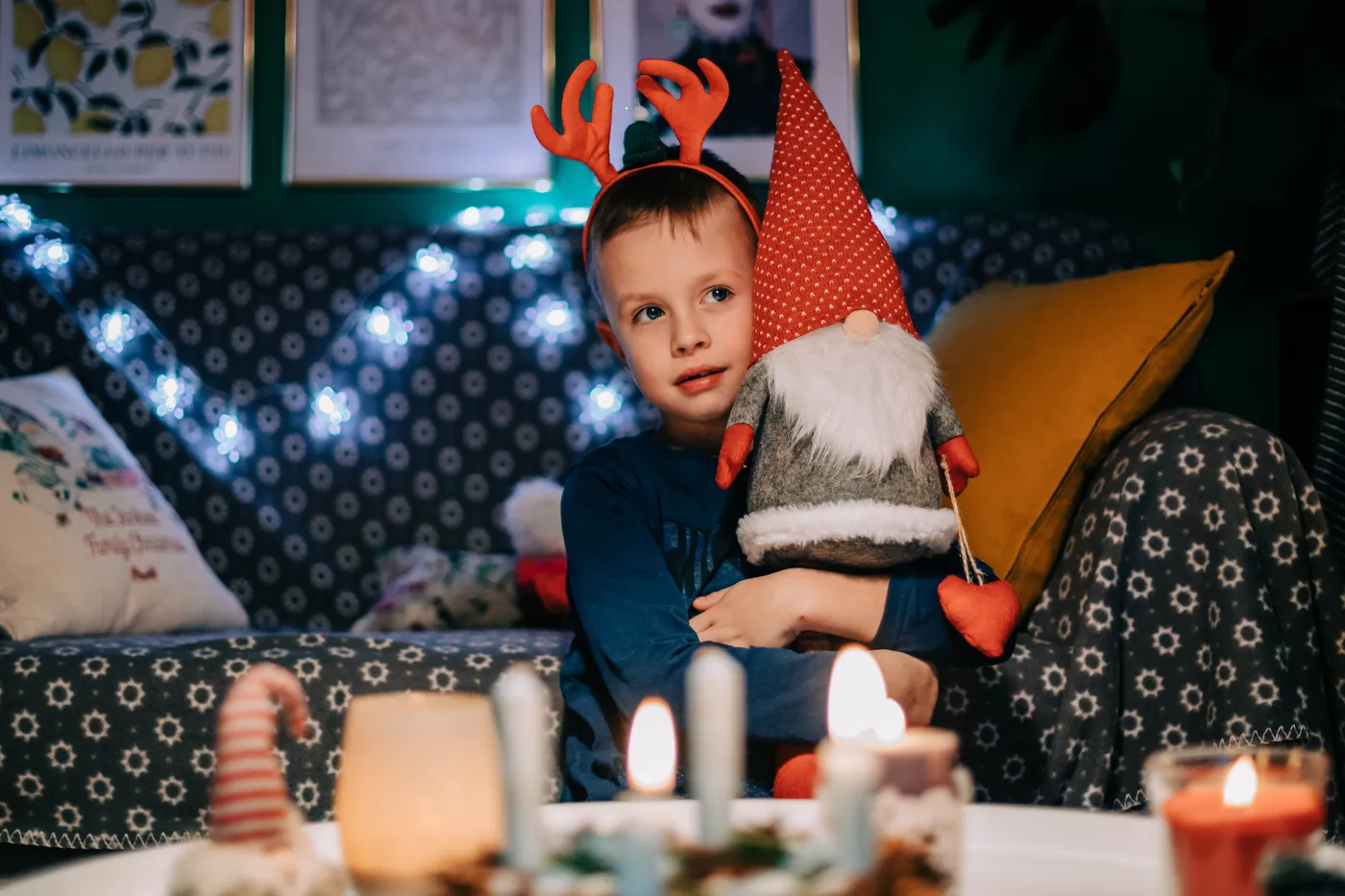 A young boy enjoying Christmas indoors, holding a gnome plush toy with festive lights.
