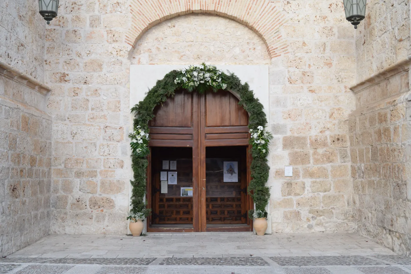 Ancient stone entrance with a wooden door adorned with greenery and white flowers.