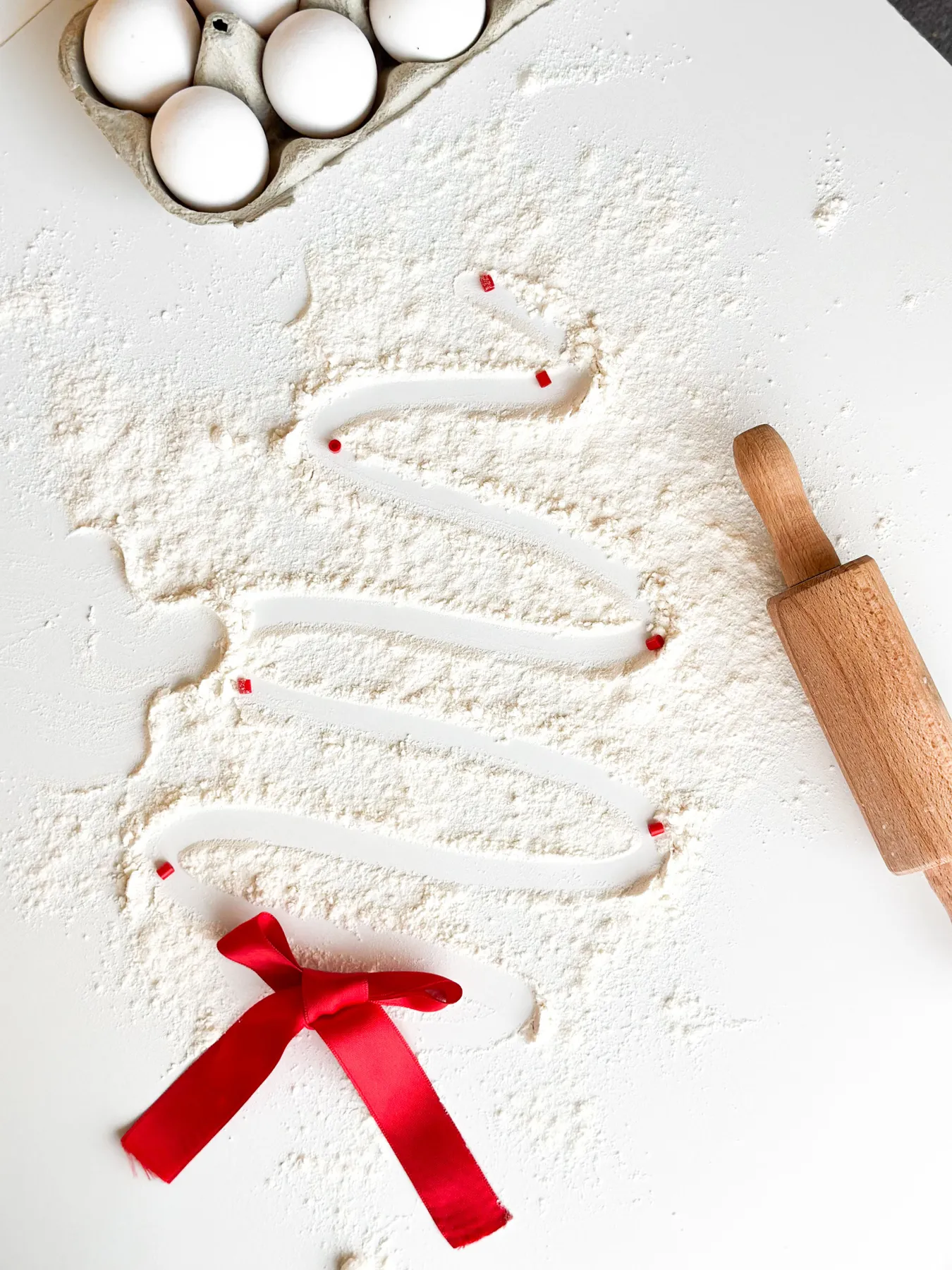 Artistic Christmas tree design with flour on baking surface, eggs, and rolling pin.