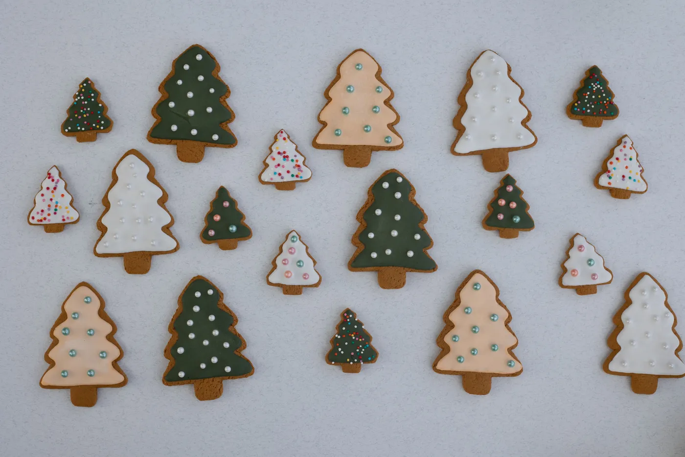 Assorted Christmas tree-shaped gingerbread cookies with colorful icing and sprinkles on a white background.