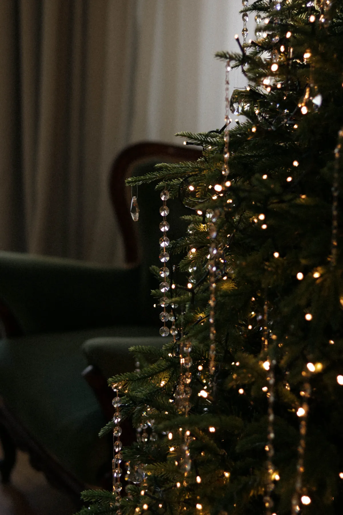 Beautifully decorated Christmas tree adorned with lights and crystal garland in a cozy living room.