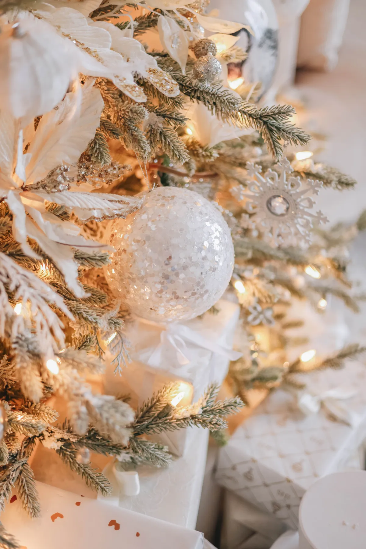 Beautifully decorated Christmas tree with lights, snowflake ornament, and wrapped gifts.