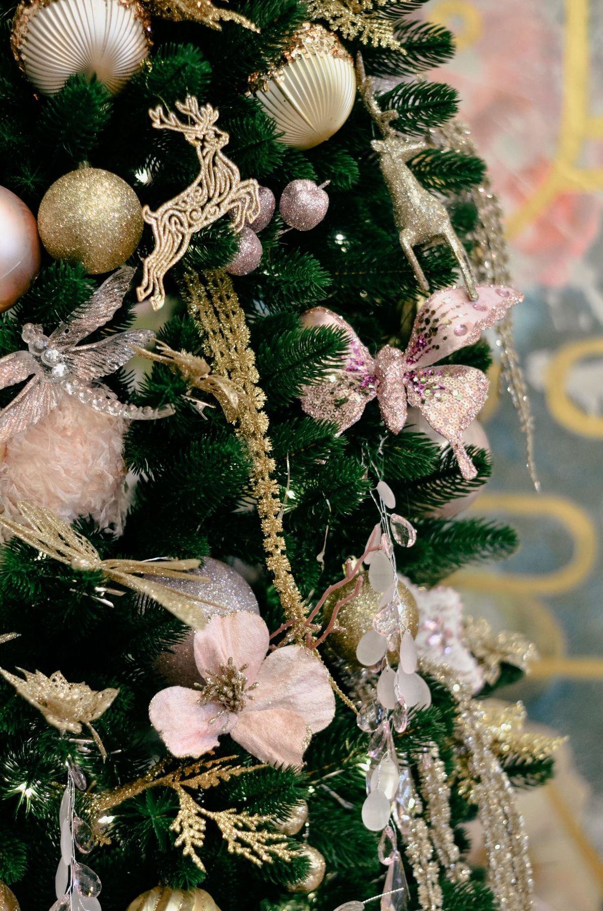 Beautifully decorated Christmas tree with gold and pink ornaments, shells, and reindeer in a festive setting.