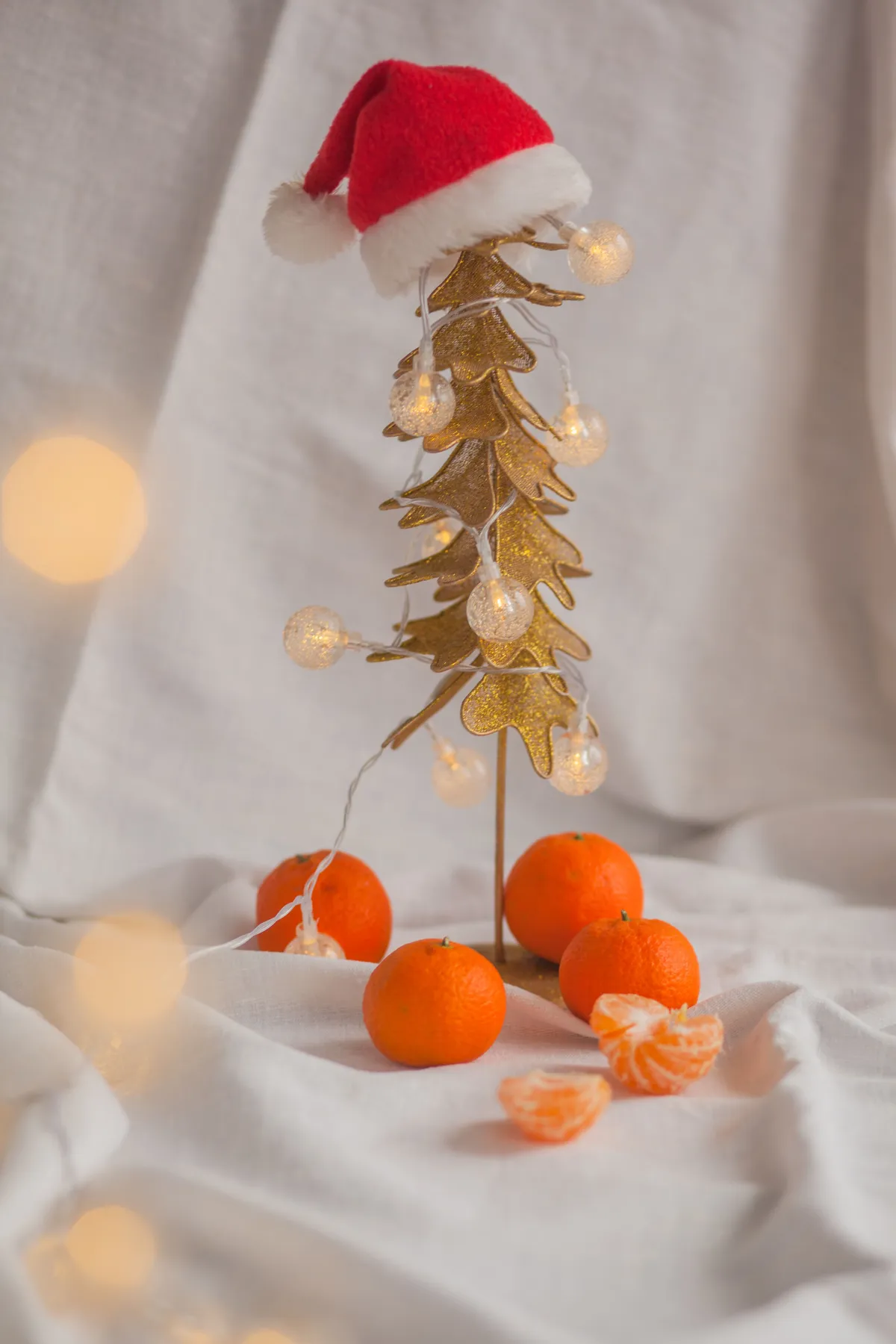 Christmas composition of bright orange mandarins around plastic toy Christmas tree with red Santa hat on top