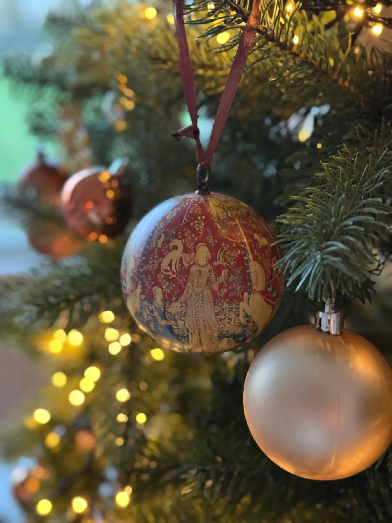 Christmas ornaments on a decorated Christmas tree. The main ornament displays a design inspired by the medieval Flemish tapestries known as ‘The Lady and the Unicorn’ (French: La Dame à la licorne), w