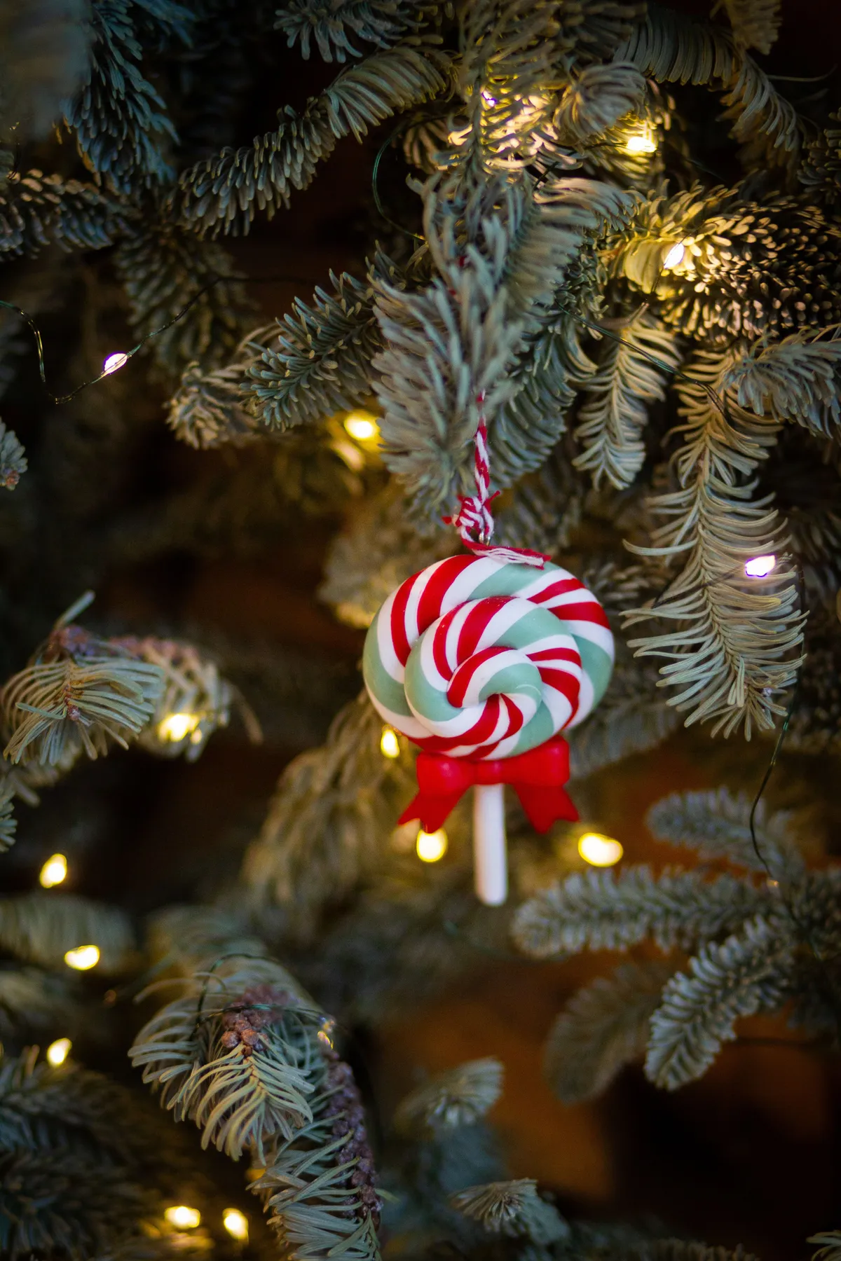 Close-up of a candy cane ornament on a decorated Christmas tree with lights.