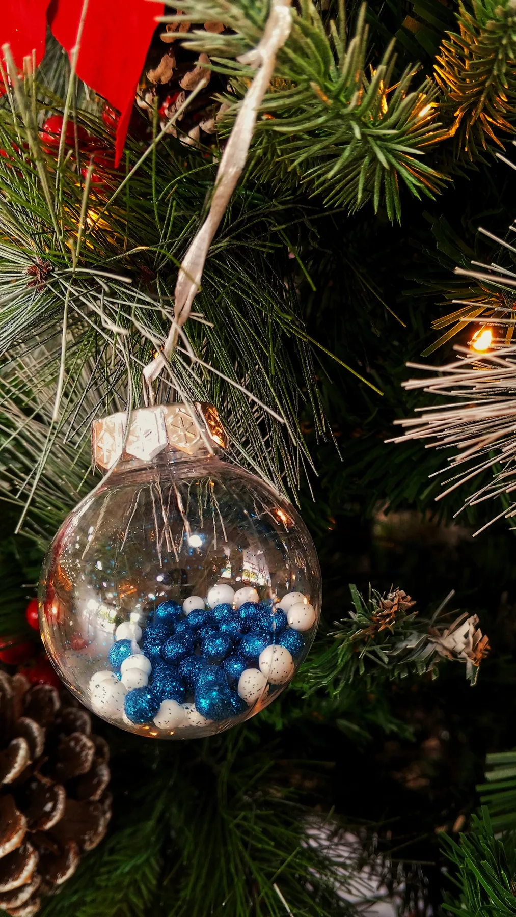 Close-up of a Christmas ornament hanging on a tree branch with seasonal decorations.