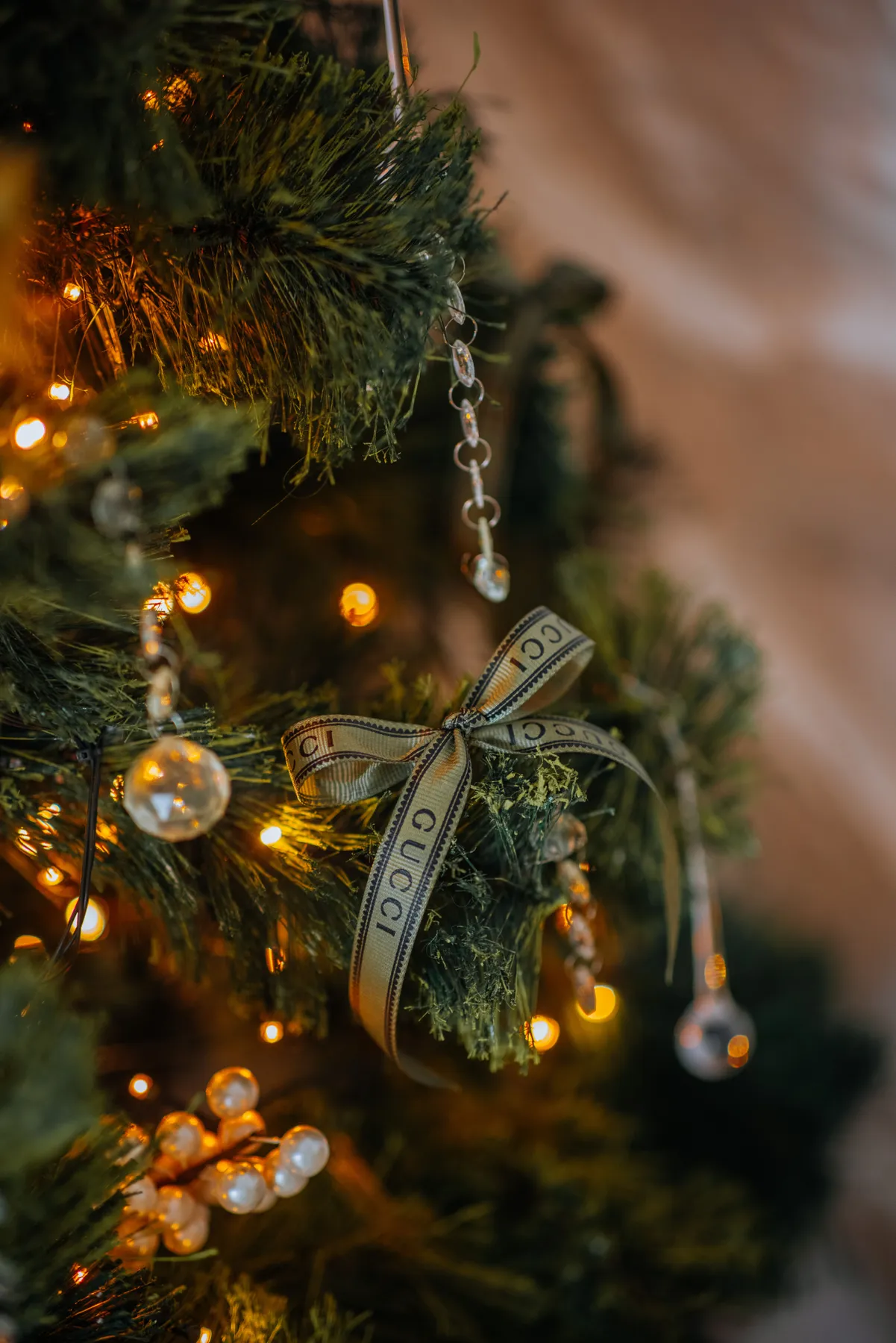 Close-up of a Christmas tree decorated with Gucci ribbon and warm lights, creating a luxurious holiday ambiance.