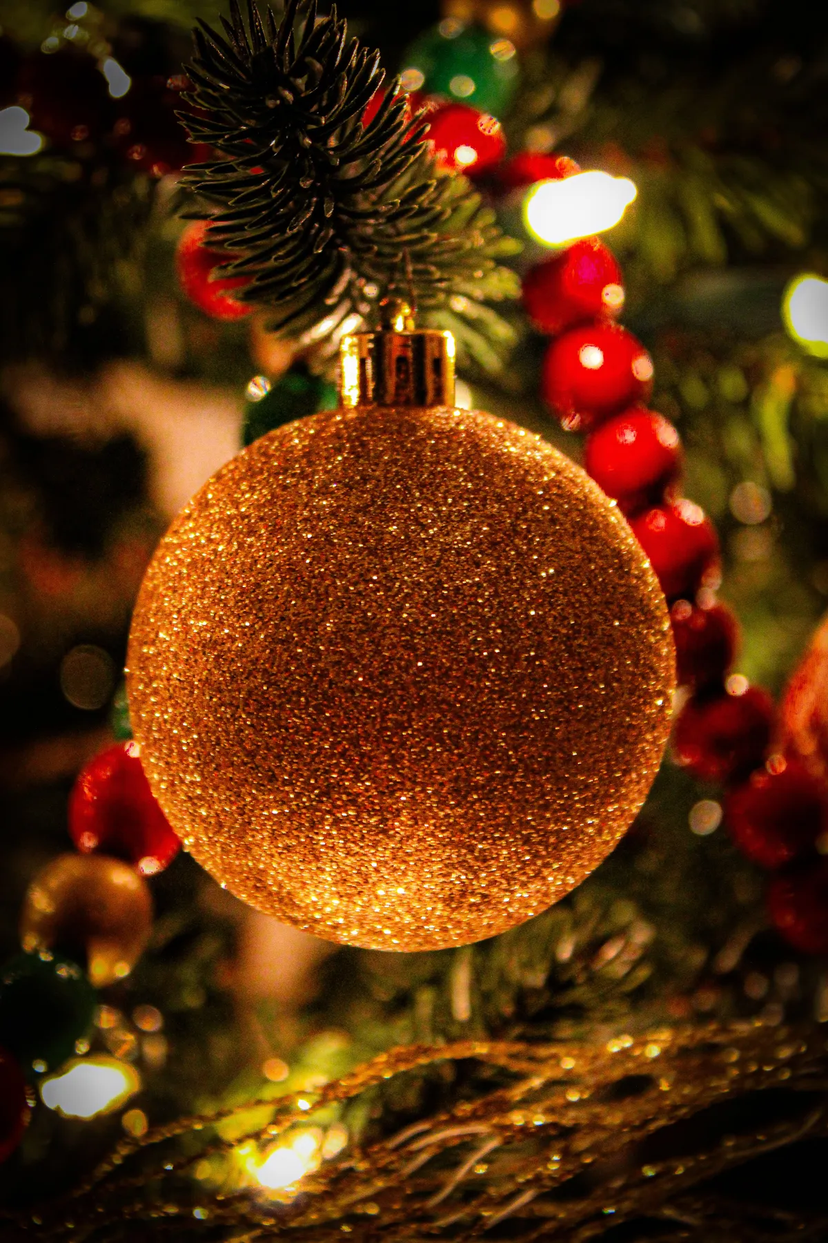 Close-up of a glittering gold ornament hanging from a festive Christmas tree.
