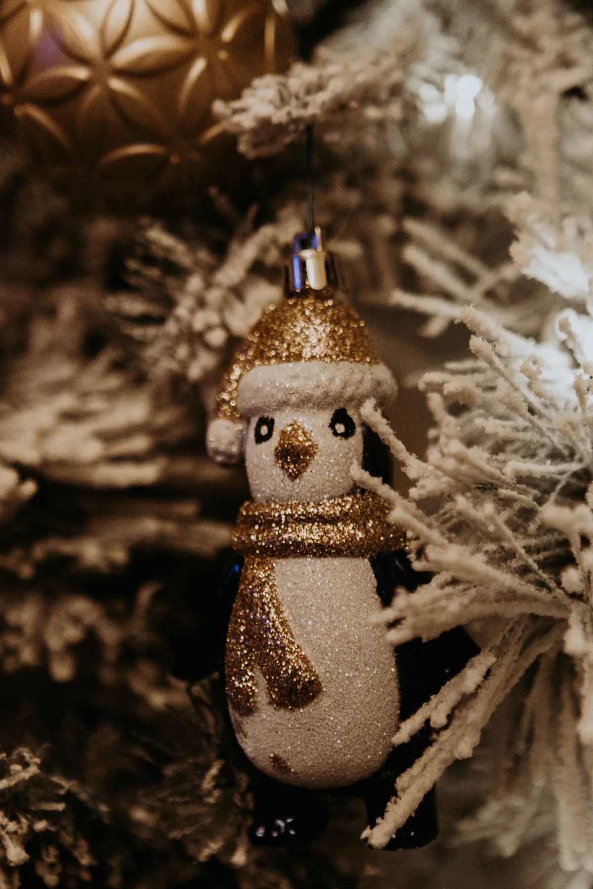Close-up of a glittery penguin ornament nestled in a snowy Christmas tree branch.