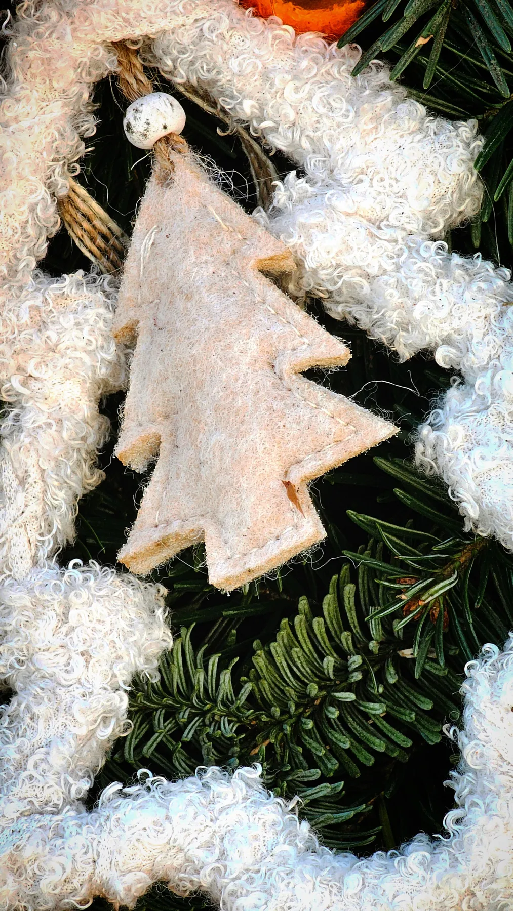Close-up of a rustic white Christmas tree ornament hanging on a pine branch, surrounded by cozy textures.