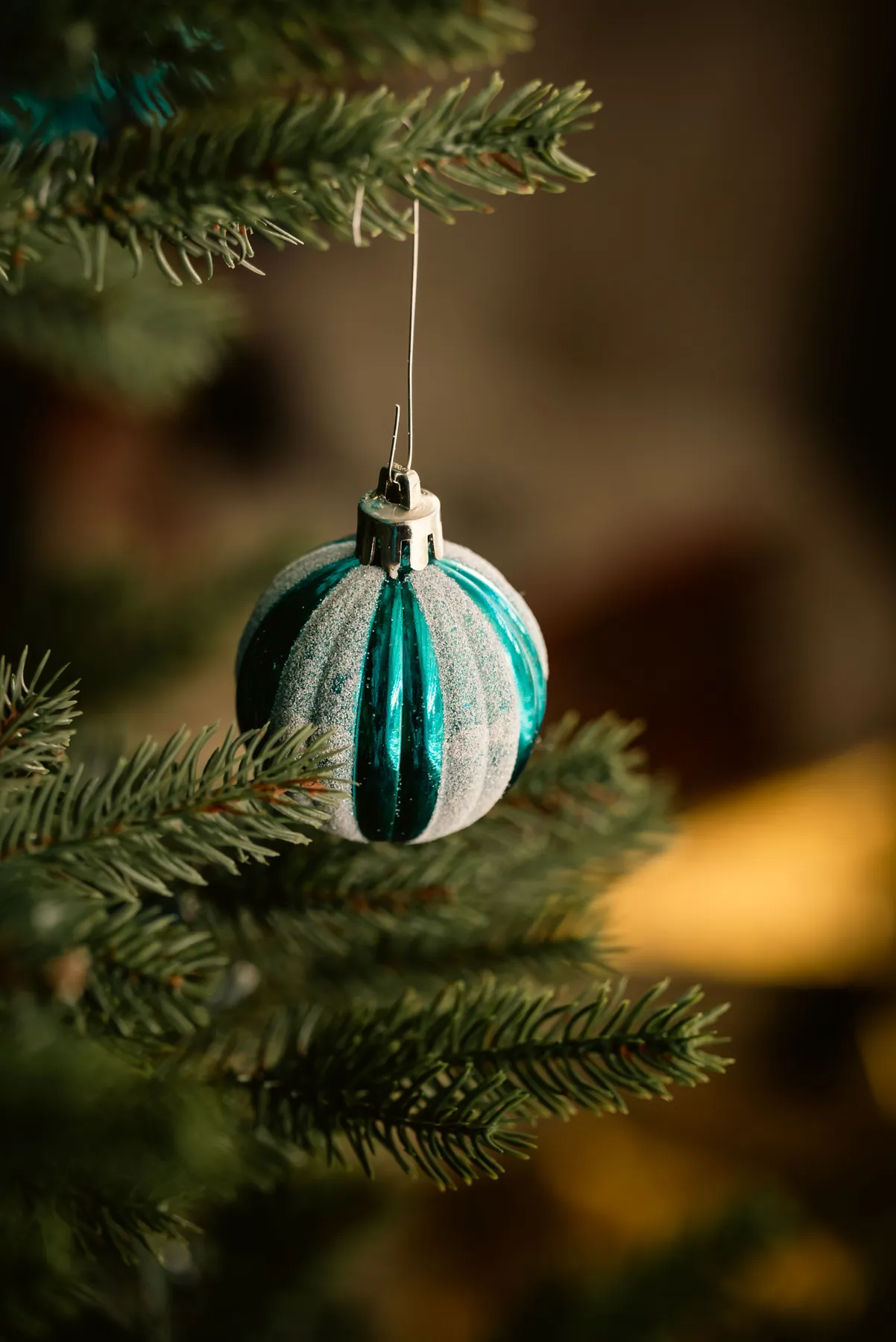 Close-up of a teal Christmas ornament hanging on a pine tree branch with a blurred background.