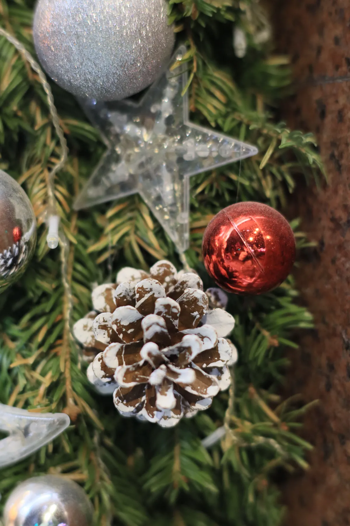 Close-up of Christmas ornaments on a tree with a snowy pine cone.