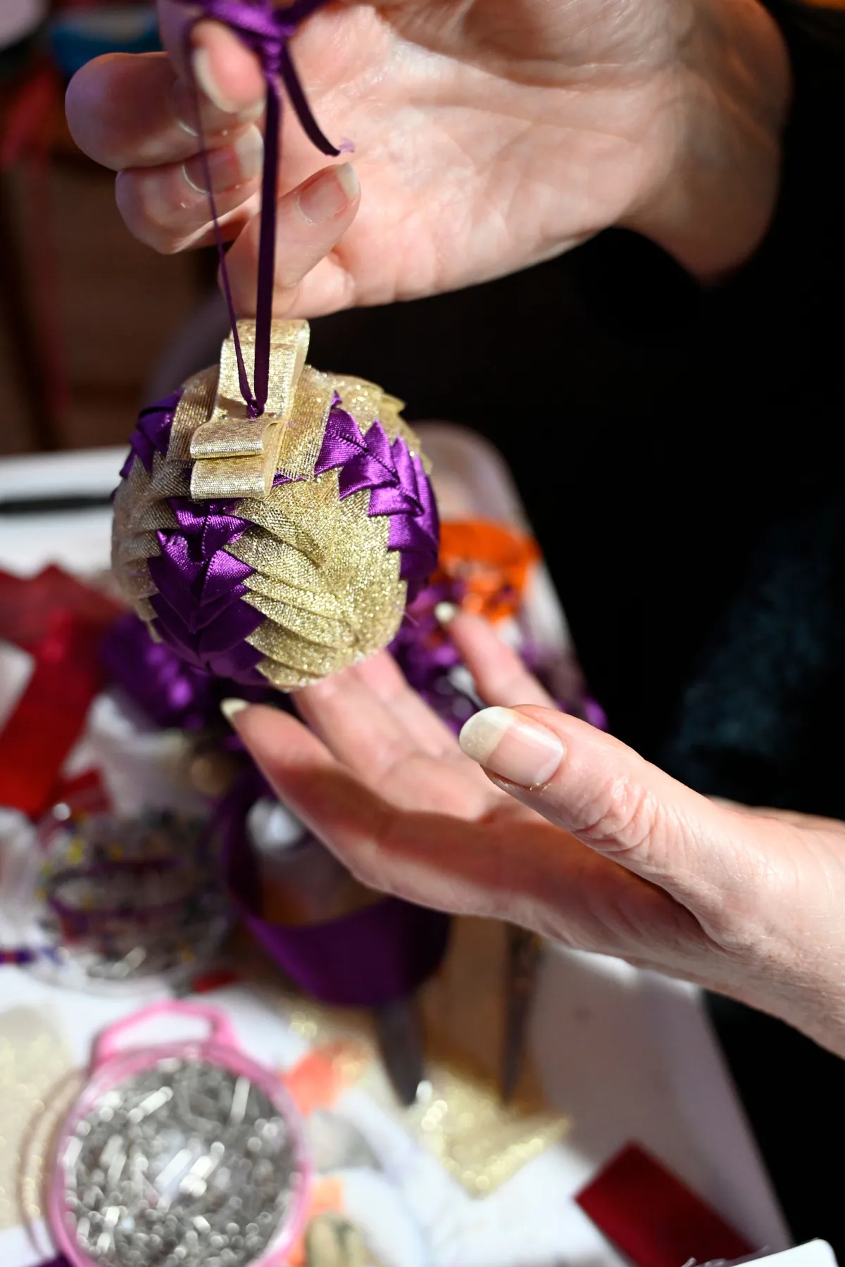 Close-up of hands crafting a decorative Christmas ornament with ribbon.