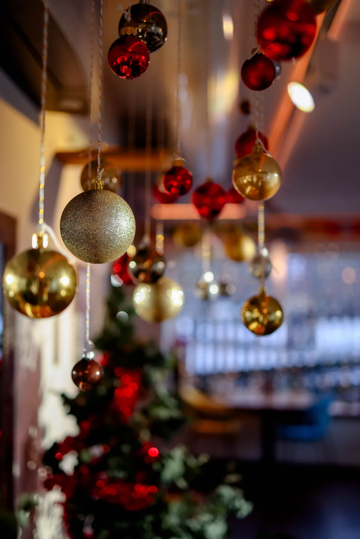 Close-up of hanging Christmas ornaments in a cozy indoor setting with blurred Christmas tree in background.