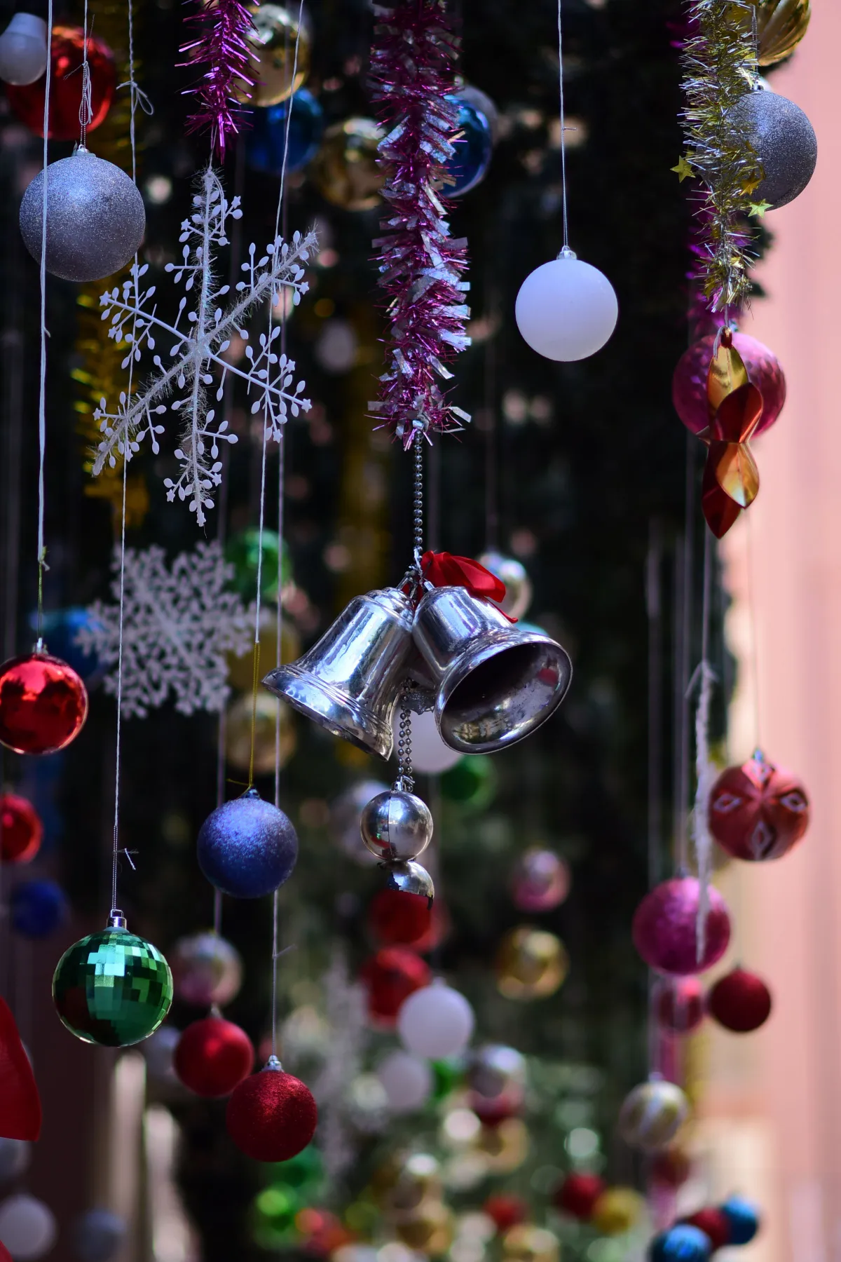 Colorful Christmas ornaments hanging from a festive display, featuring bells, baubles, and snowflakes.
