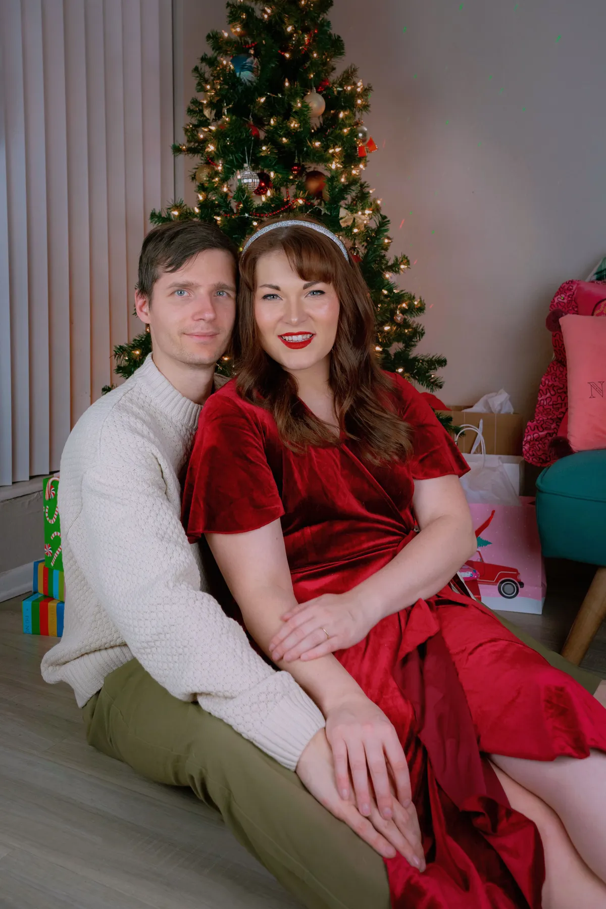 Couple in cozy holiday outfits enjoying Christmas by the decorated tree.