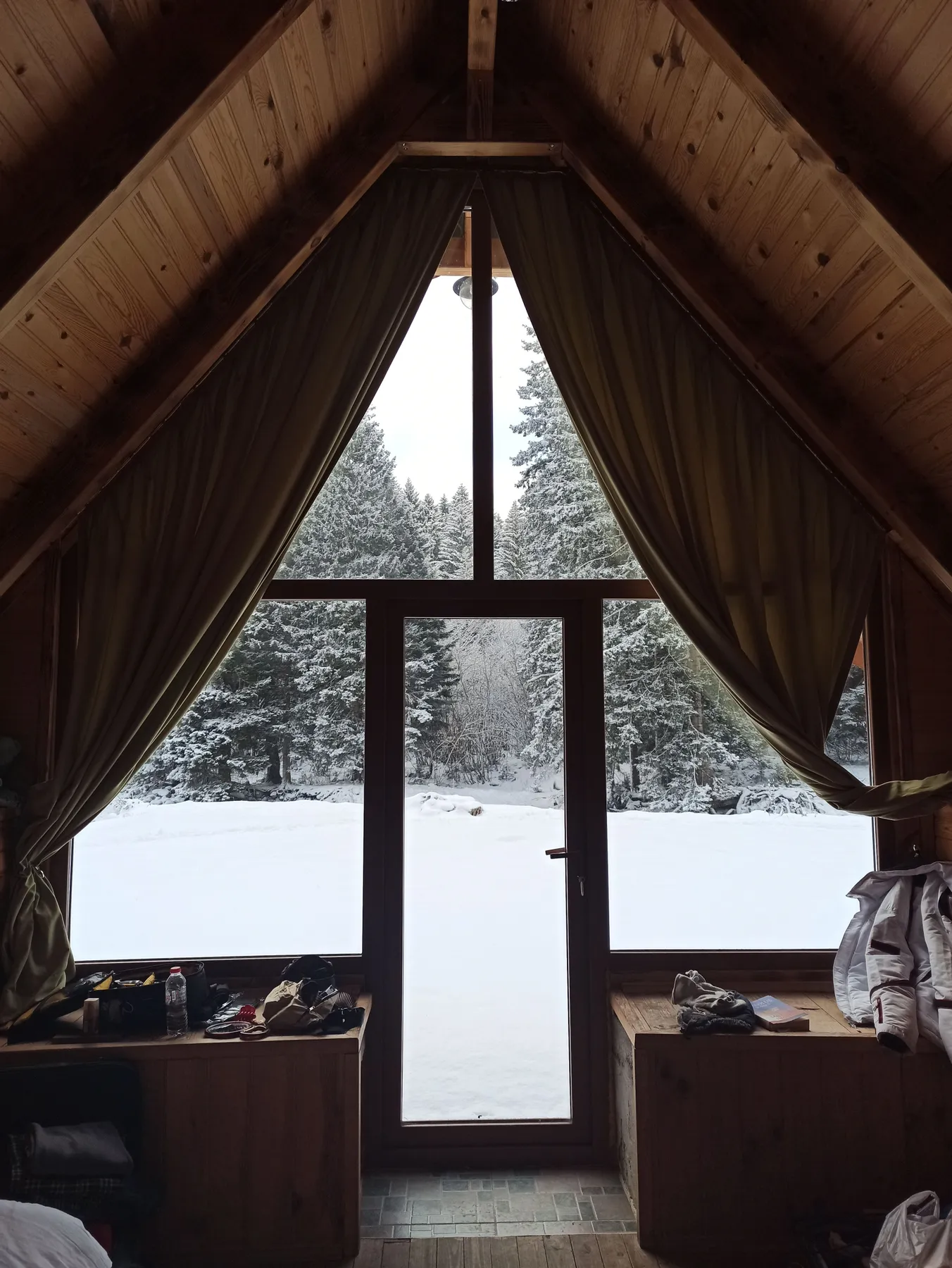 Cozy cabin interior overlooking a snowy forest through large windows.