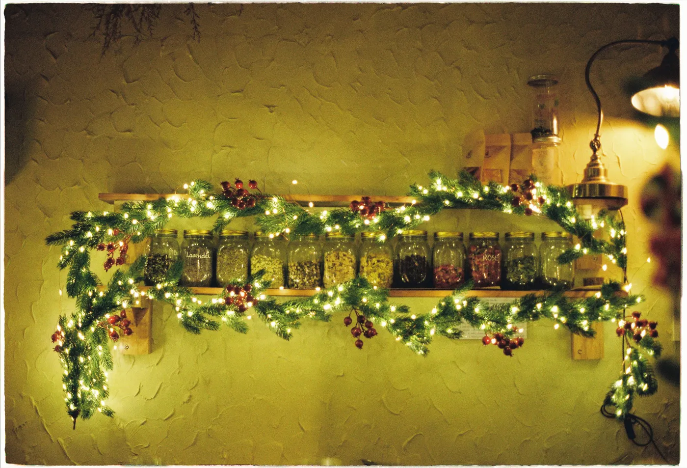 Cozy kitchen shelf decorated with Christmas garland, fairy lights, and spice jars. Perfect for holiday warmth.