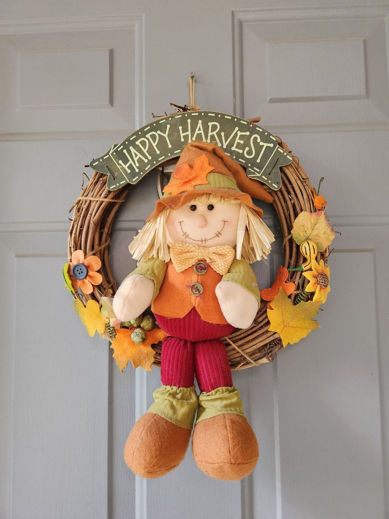 Decorative autumn wreath with a cheerful scarecrow and fall leaves, perfect for welcoming guests.