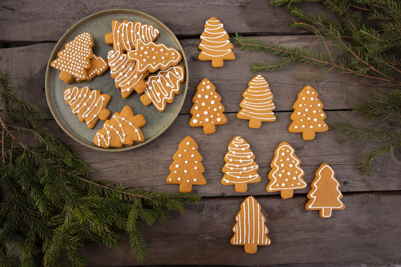Decorative gingerbread Christmas tree cookies arranged on a wooden table with green branches.