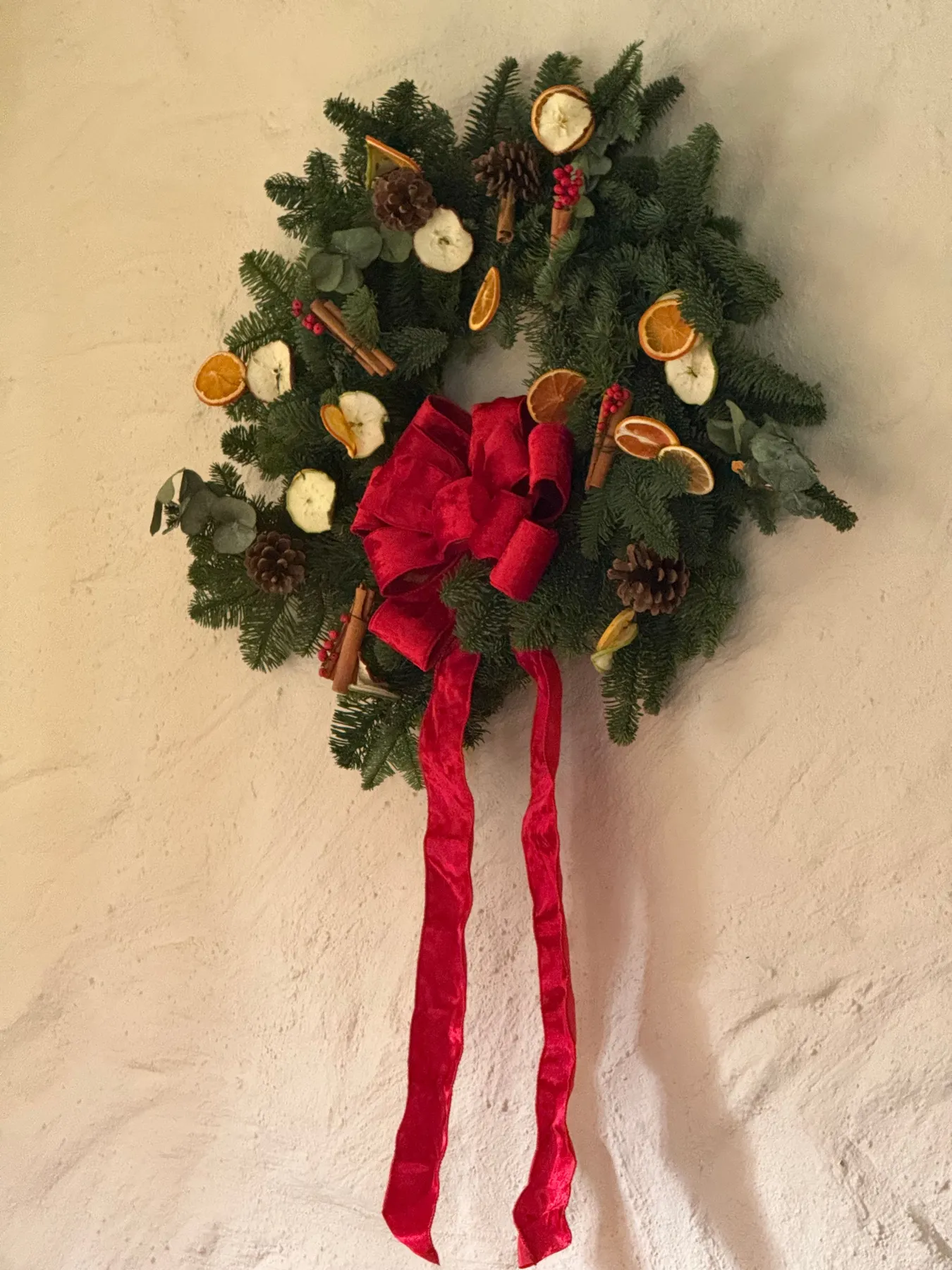 Elegant Christmas wreath adorned with dried oranges, pine cones, and red bow, perfect for holiday decor.