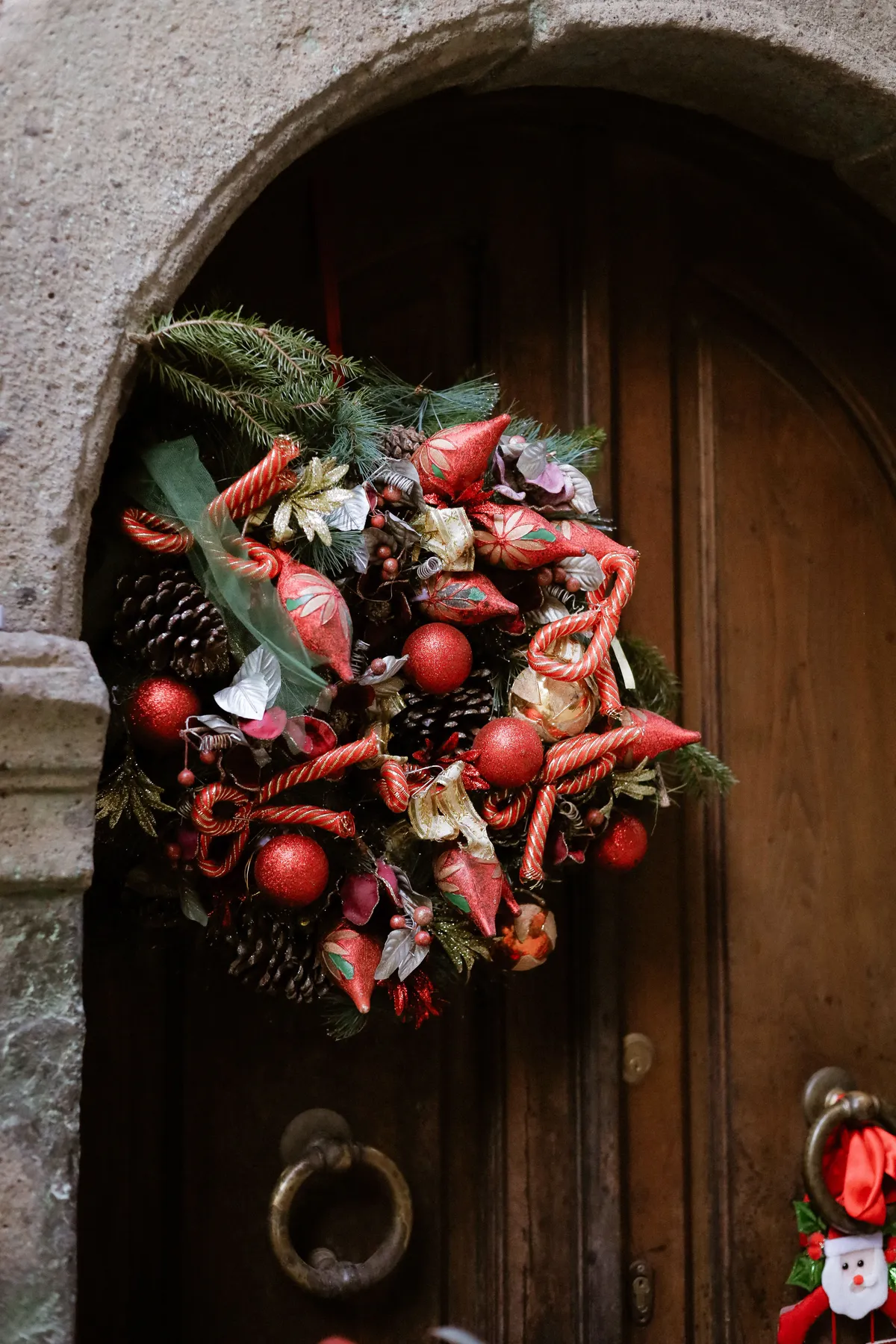 Elegant Christmas wreath on a wooden door, featuring pine cones and red ornaments.