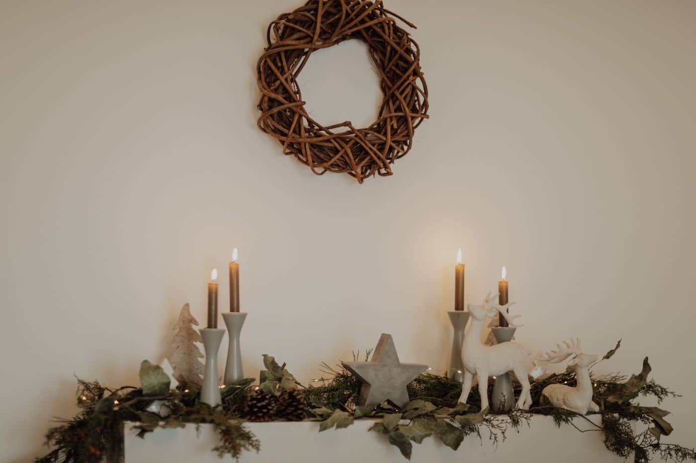 Elegant holiday mantle with candles and rustic wreath in warm lighting.