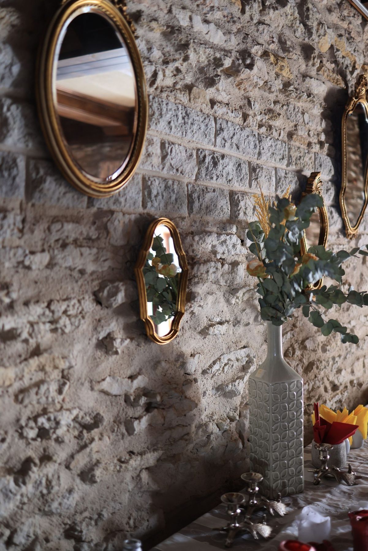 Elegant vintage mirrors and a vase adorn a rustic stone wall, creating a warm decor setting.